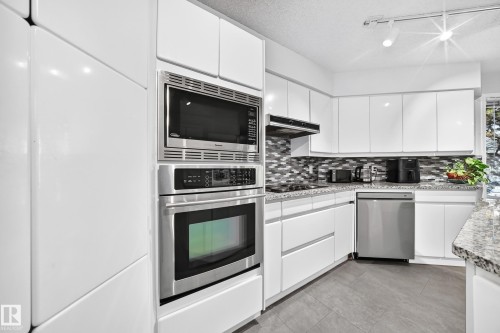 White flat-panel cabinetry with stainless steel appliances, mosaic tile backsplash, grey tile flooring, and track lighting - 5830 181 Street Nw, Edmonton, AB 