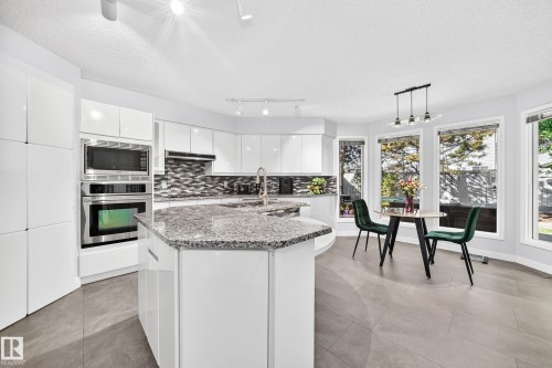 Kitchen featuring a large island with stone countertops, built-in stainless steel appliances, white cabinetry, and a mosaic tile backsplash - 5830 181 Street Nw, Edmonton, AB 