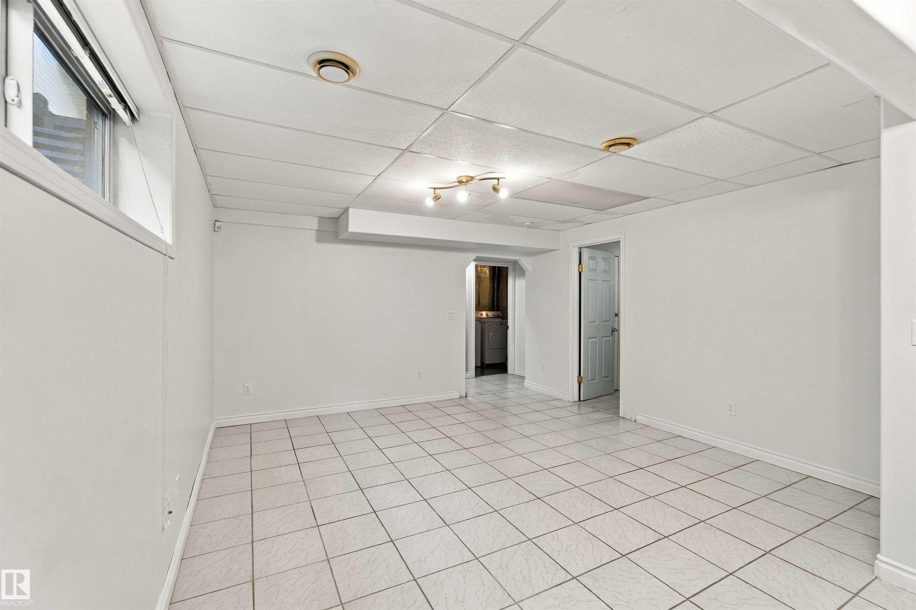 Expansive room with white tile flooring, drop ceiling, and a large window - 3524 Mclean Crescent Sw, Edmonton, AB