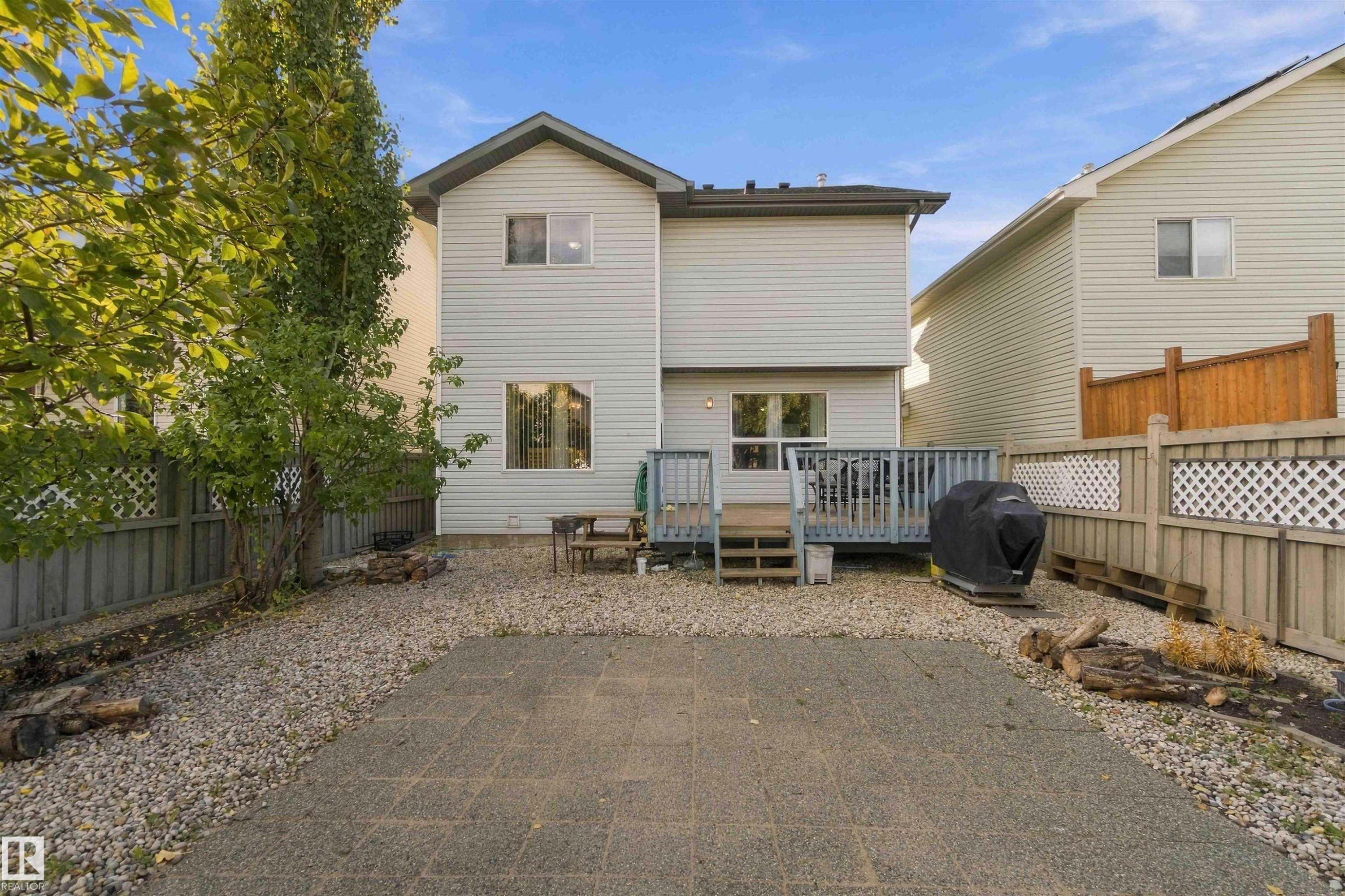 Rear exterior featuring light-colored siding, a multi-level deck, and a stone patio - 3524 Mclean Crescent Sw, Edmonton, AB