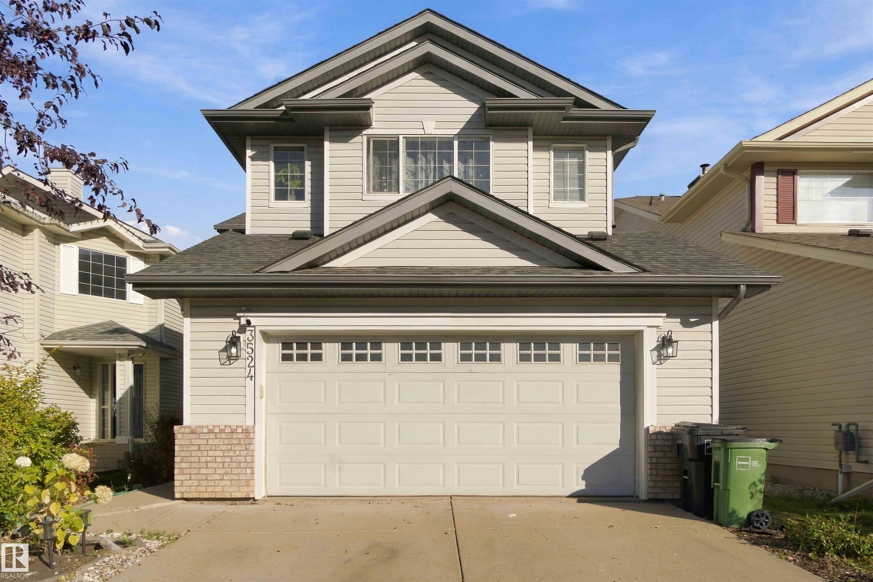 Two-story residence featuring light-toned horizontal siding, a prominent attached garage with panel windows, and a dark shingled roof - 3524 Mclean Crescent Sw, Edmonton, AB