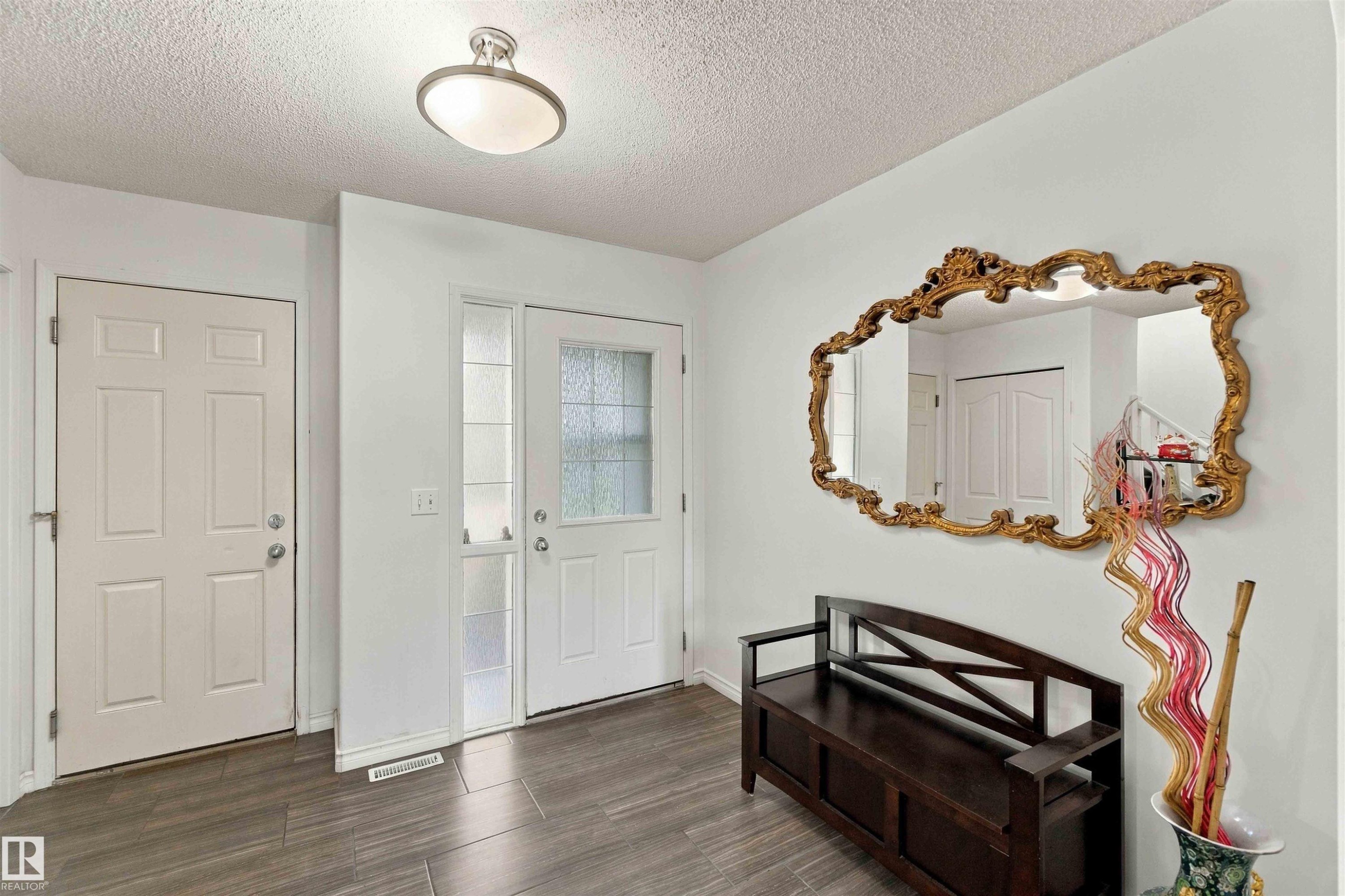 Wood-finish flooring with a white six-panel door, front entry door with privacy glass, and a flush mount ceiling light - 3524 Mclean Crescent Sw, Edmonton, AB