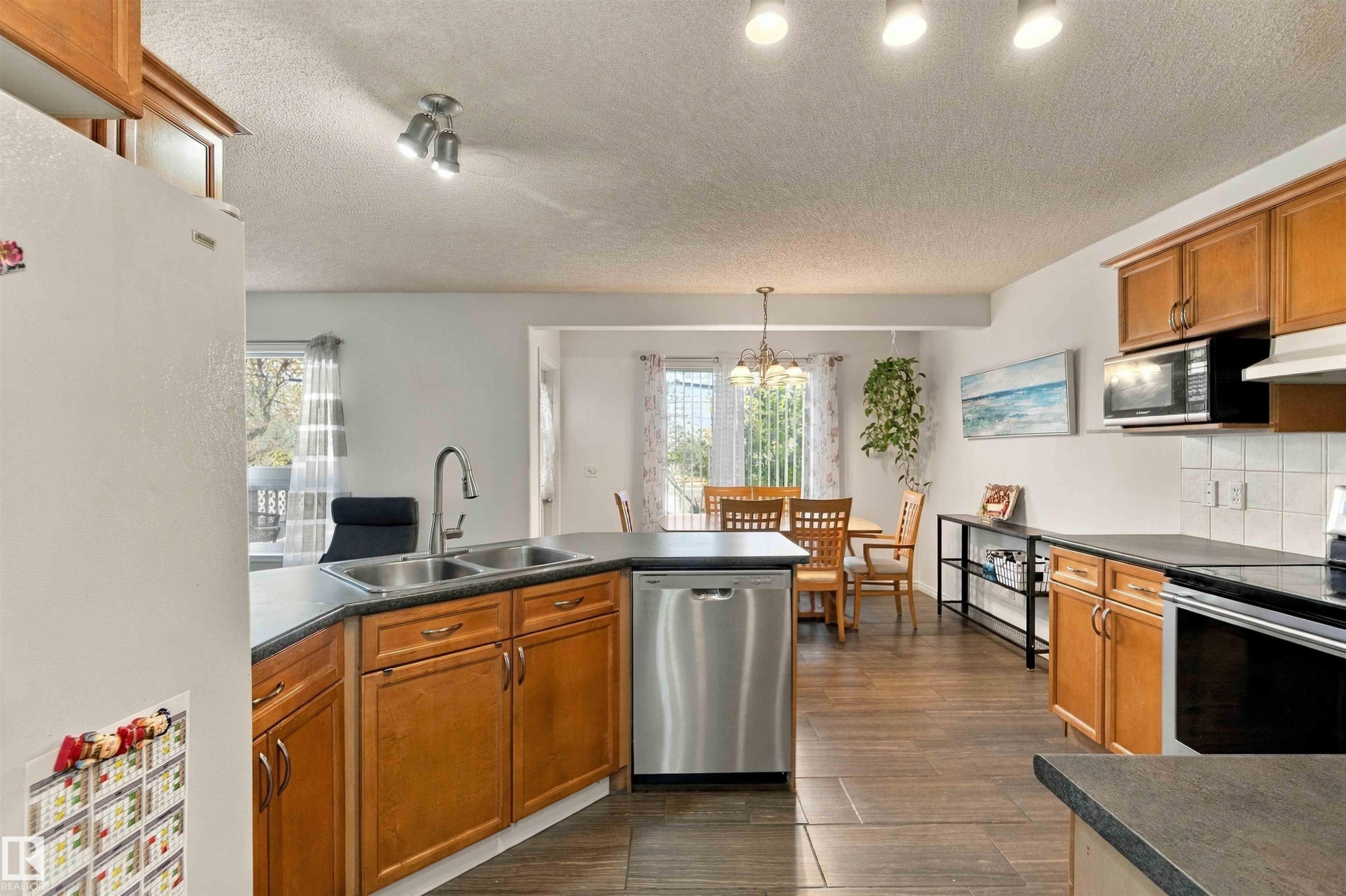 Kitchen featuring wood cabinetry, stainless steel appliances, and dark countertops - 3524 Mclean Crescent Sw, Edmonton, AB