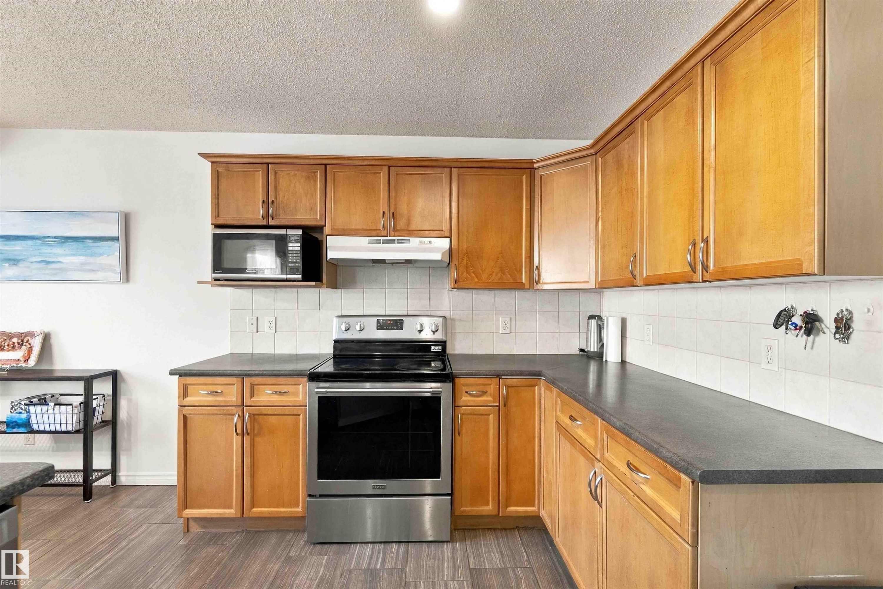 Kitchen featuring wood-finish cabinetry, dark countertops, white tile backsplash, and wood-finish flooring - 3524 Mclean Crescent Sw, Edmonton, AB
