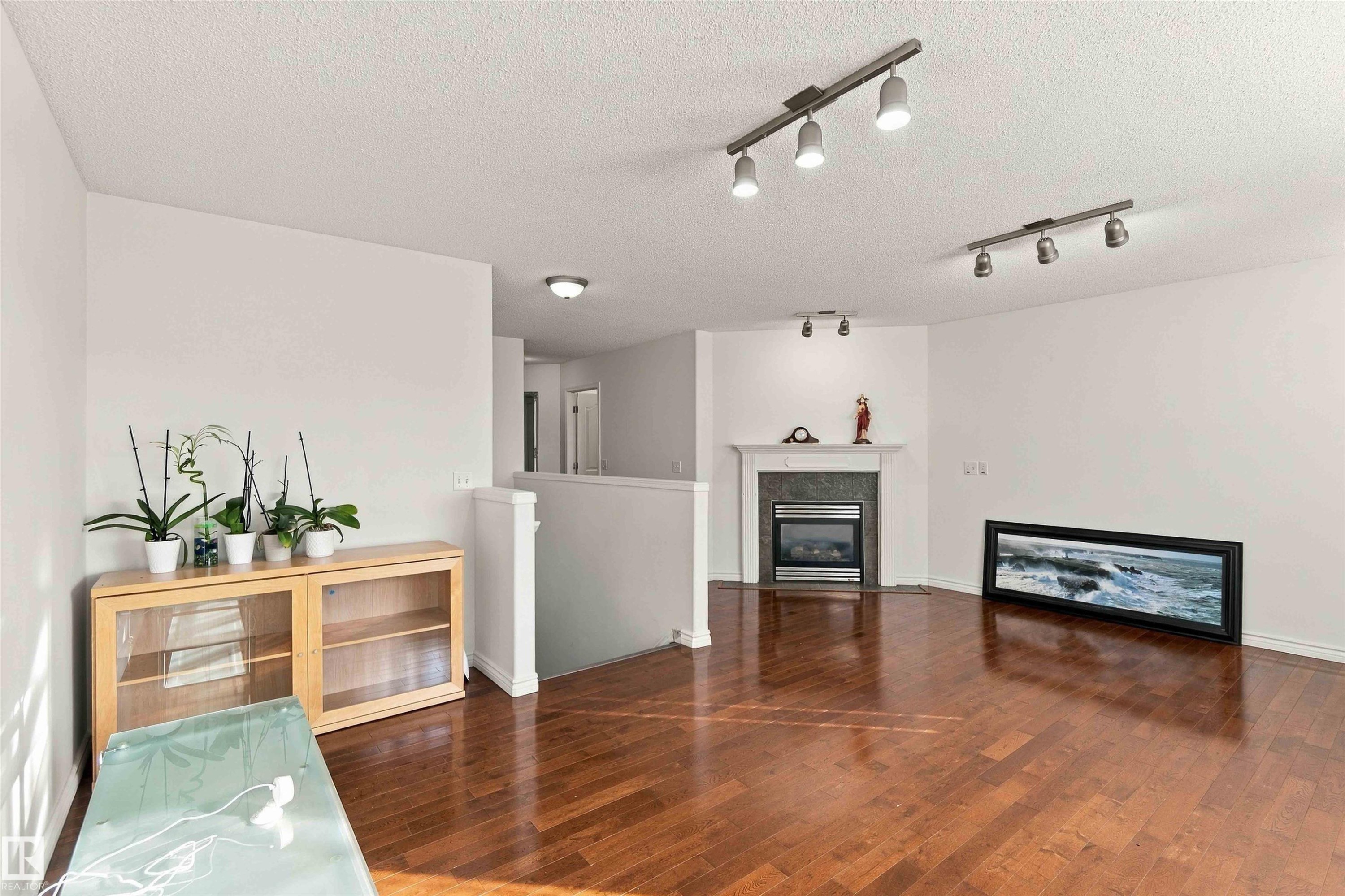 Hardwood-finish flooring, built-in fireplace with stone surround and white mantle, track lighting fixtures, and a white painted railing - 3524 Mclean Crescent Sw, Edmonton, AB