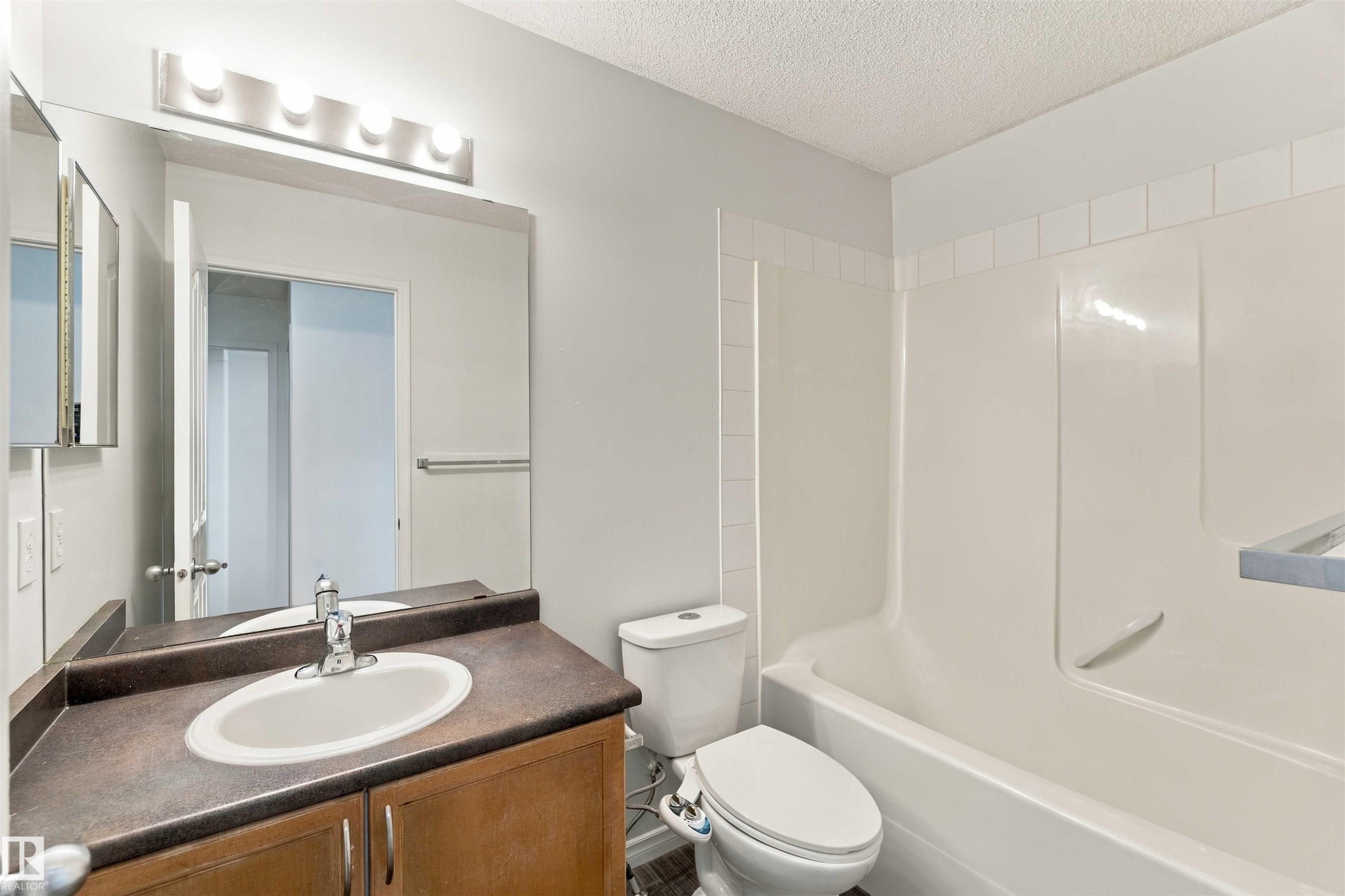 Bathroom featuring a wood-finish vanity with a surface-mounted sink, a large wall mirror, a built-in medicine cabinet, a toilet, and a bathtub with a tiled surround - 3524 Mclean Crescent Sw, Edmonton, AB