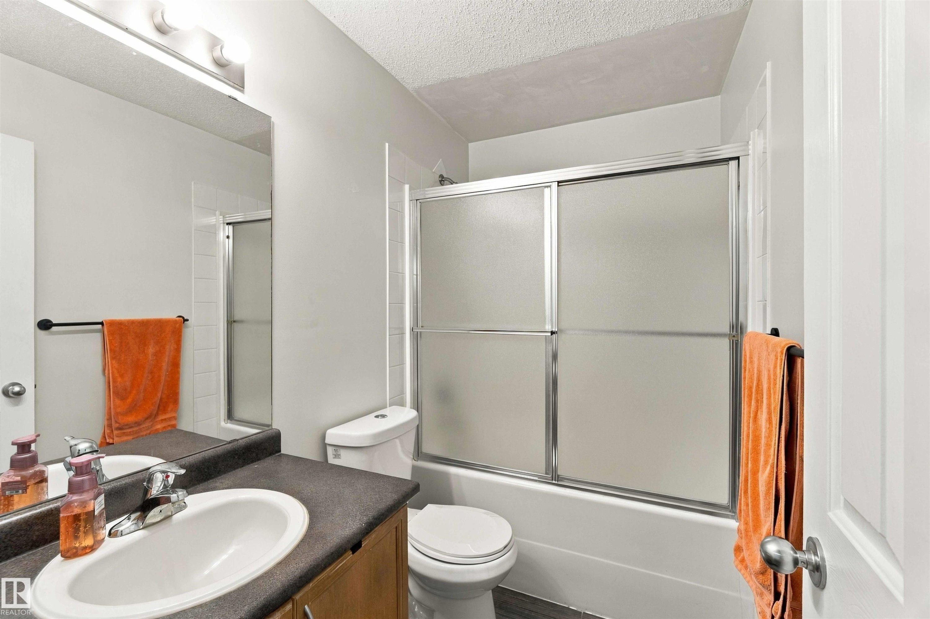 Bathroom featuring a vanity with an integrated sink, a rectangular mirror, a three-light fixture, and a bathtub with sliding shower doors - 3524 Mclean Crescent Sw, Edmonton, AB