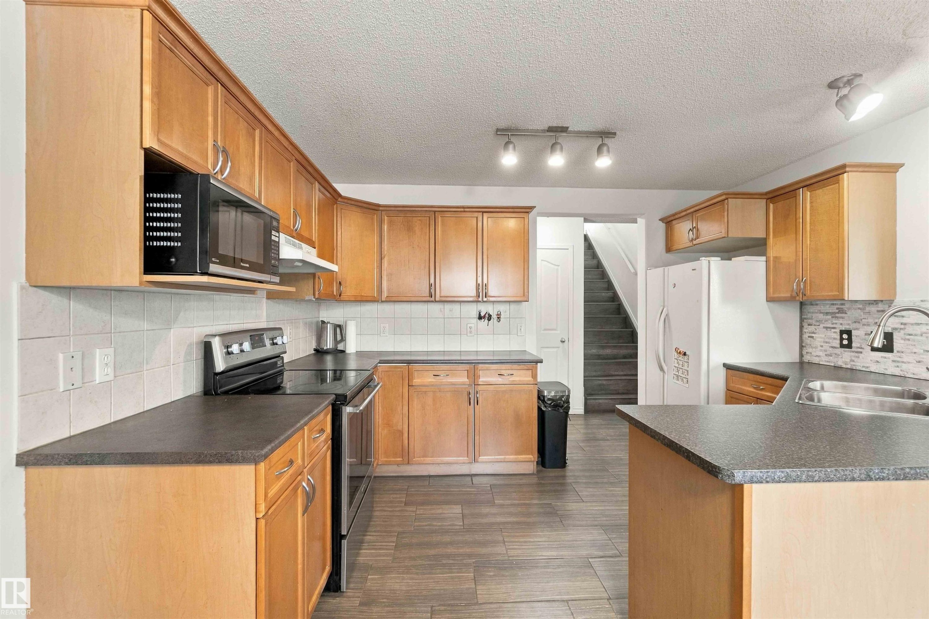 Expansive kitchen featuring light wood cabinetry, dark countertops, built-in stainless steel appliances, and wood-finish flooring - 3524 Mclean Crescent Sw, Edmonton, AB