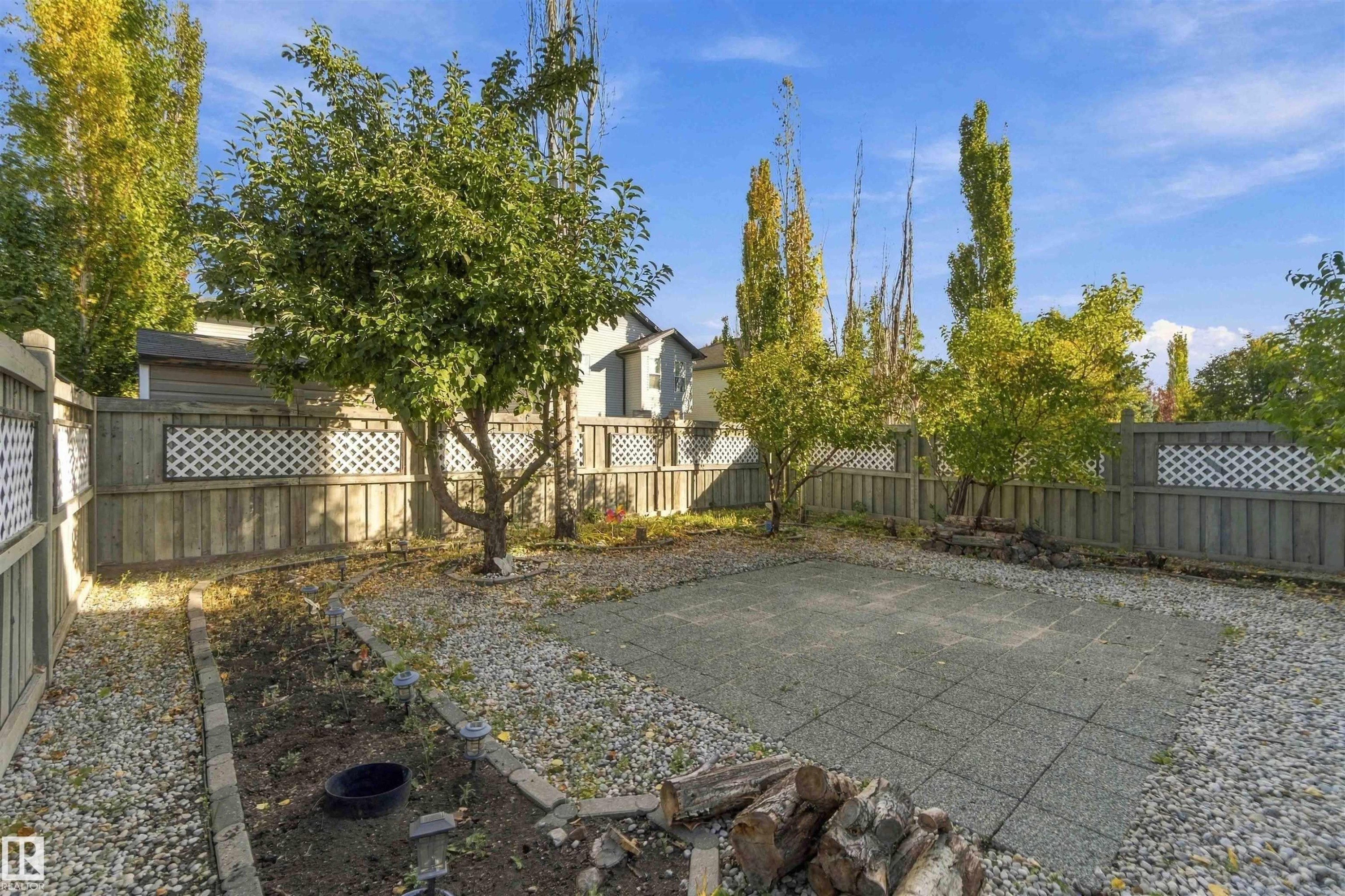 Enclosed backyard featuring a paved patio area, gravel perimeter, a garden bed, and mature trees - 3524 Mclean Crescent Sw, Edmonton, AB