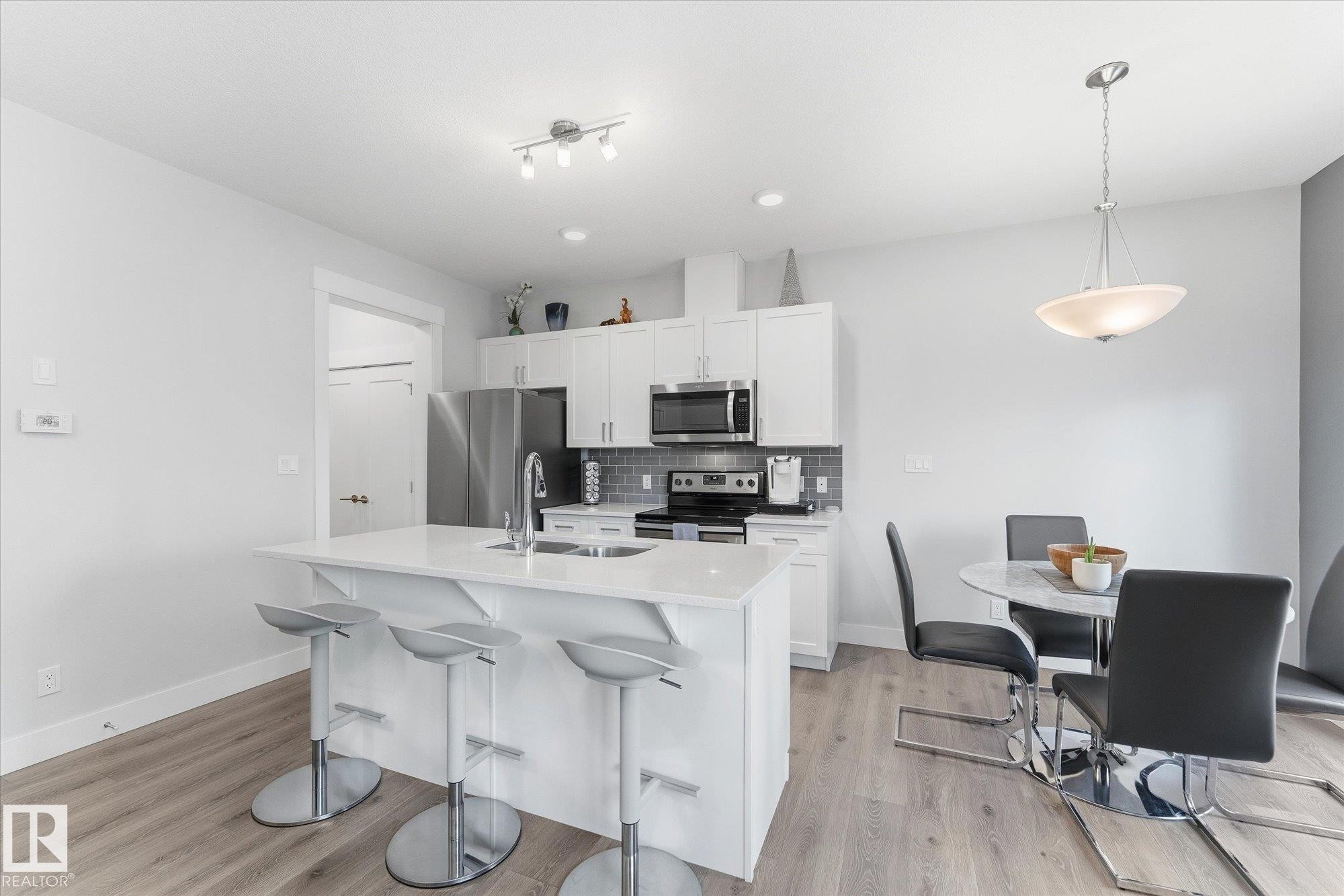 Kitchen featuring white cabinetry, stainless steel appliances, a grey subway tile backsplash, a kitchen island with seating, and wood-finish flooring - #15 4835 Wright Dr Sw, Edmonton, AB