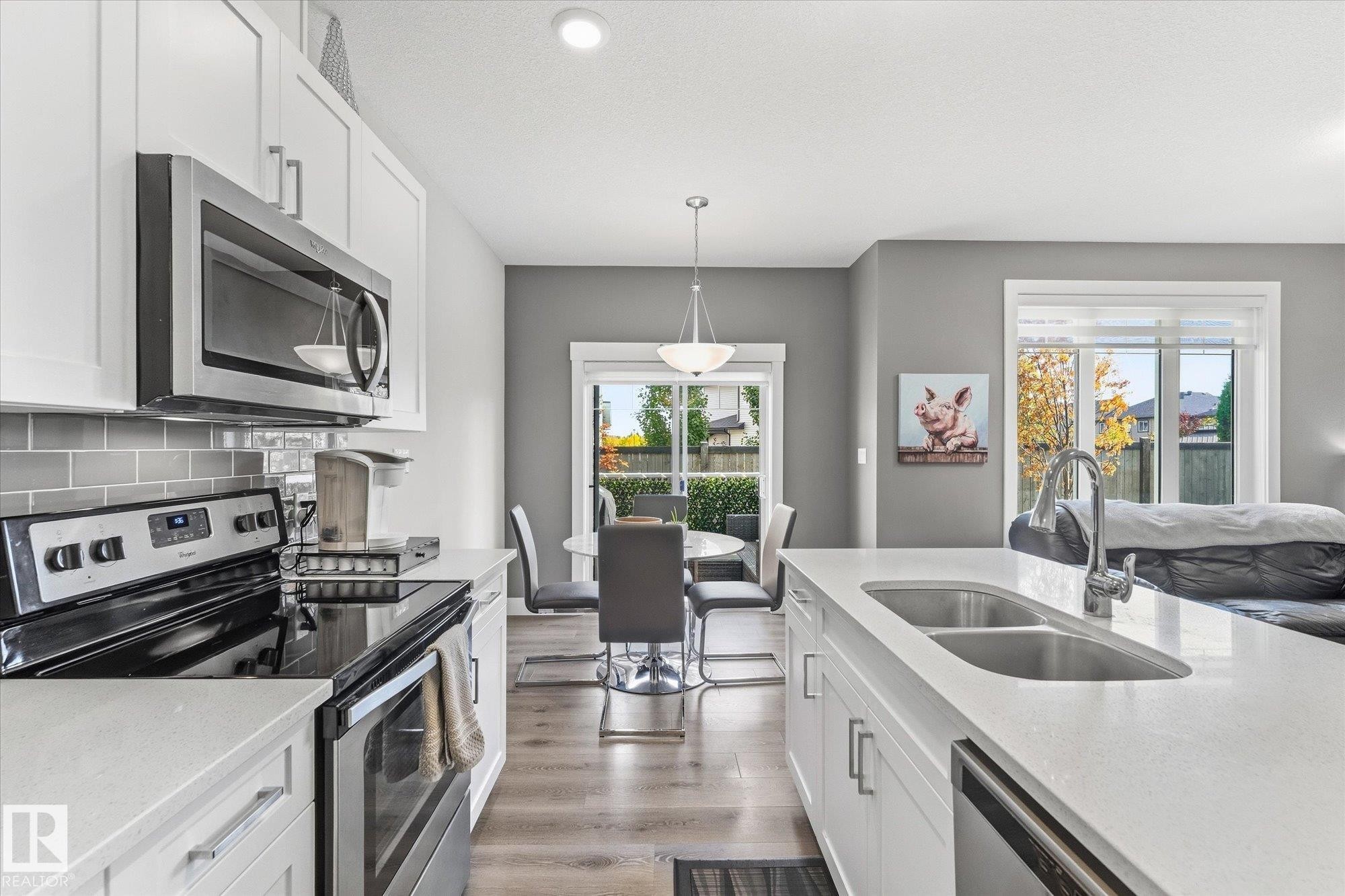 White cabinetry, stainless steel appliances, stone countertops, gray subway tile backsplash, and wood-finish flooring - #15 4835 Wright Dr Sw, Edmonton, AB