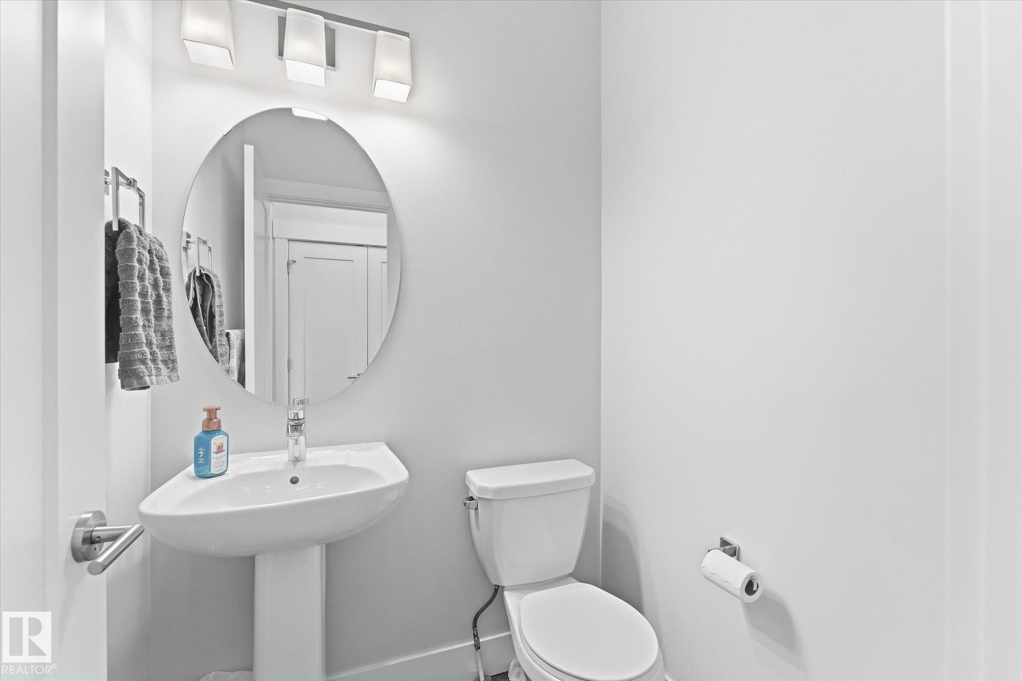 Pedestal sink, wall-mounted mirror, modern overhead lighting, white toilet, and chrome fixtures - #15 4835 Wright Dr Sw, Edmonton, AB