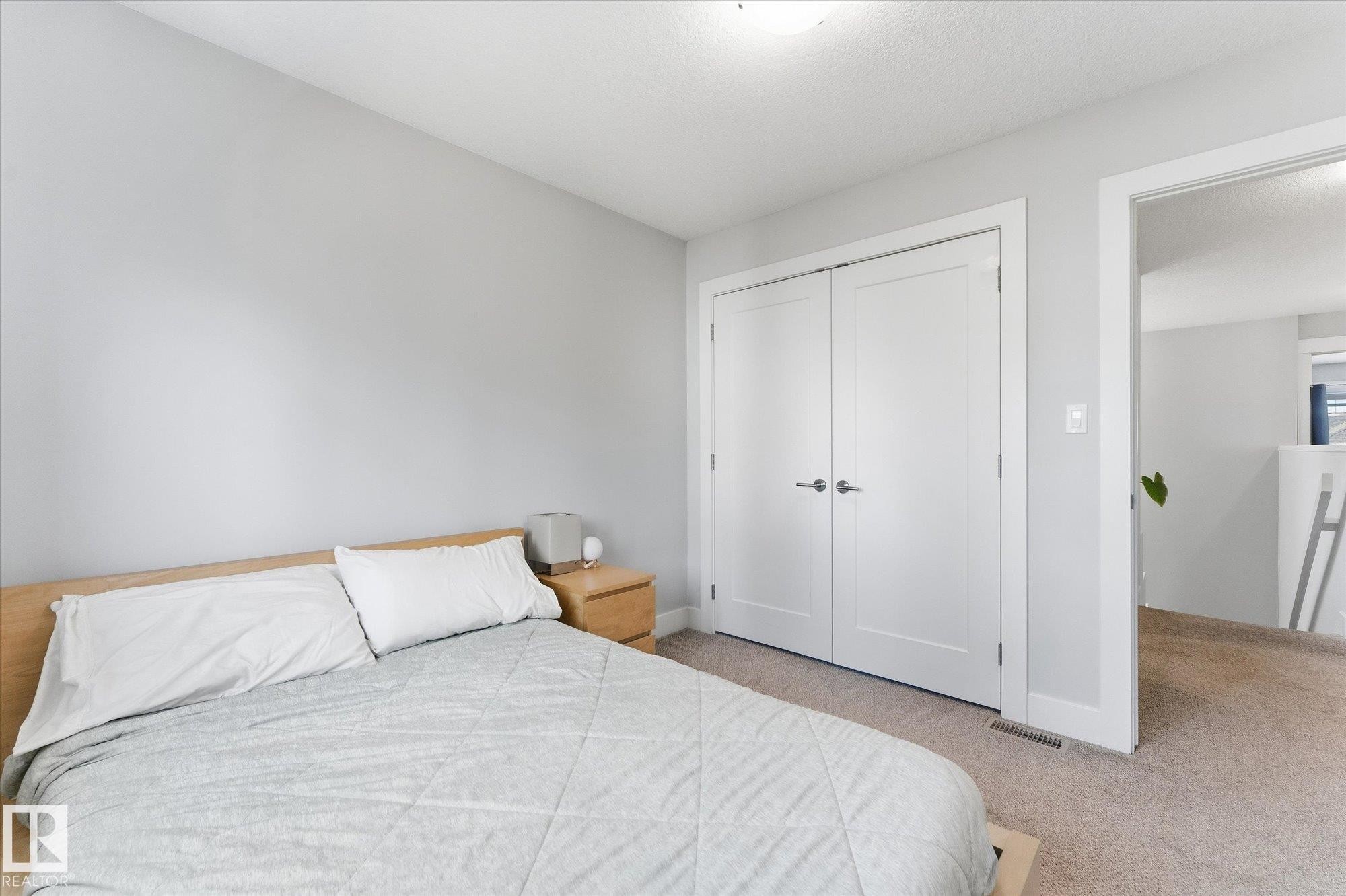 Soft gray walls with white trim, light-colored wood-finish headboard, and dual white paneled doors - #15 4835 Wright Dr Sw, Edmonton, AB