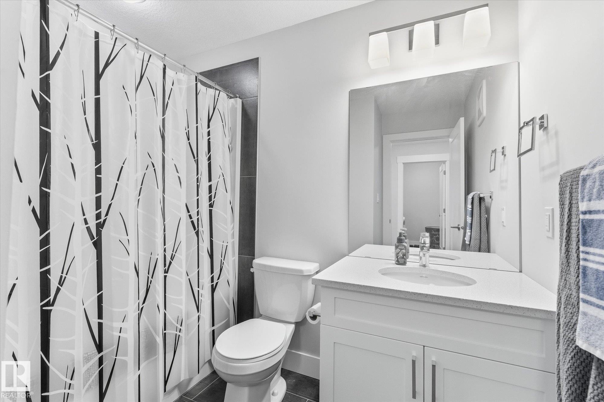 White vanity with an integrated sink and chrome faucet, full-width mirror, and a wall-mounted light fixture - #15 4835 Wright Dr Sw, Edmonton, AB