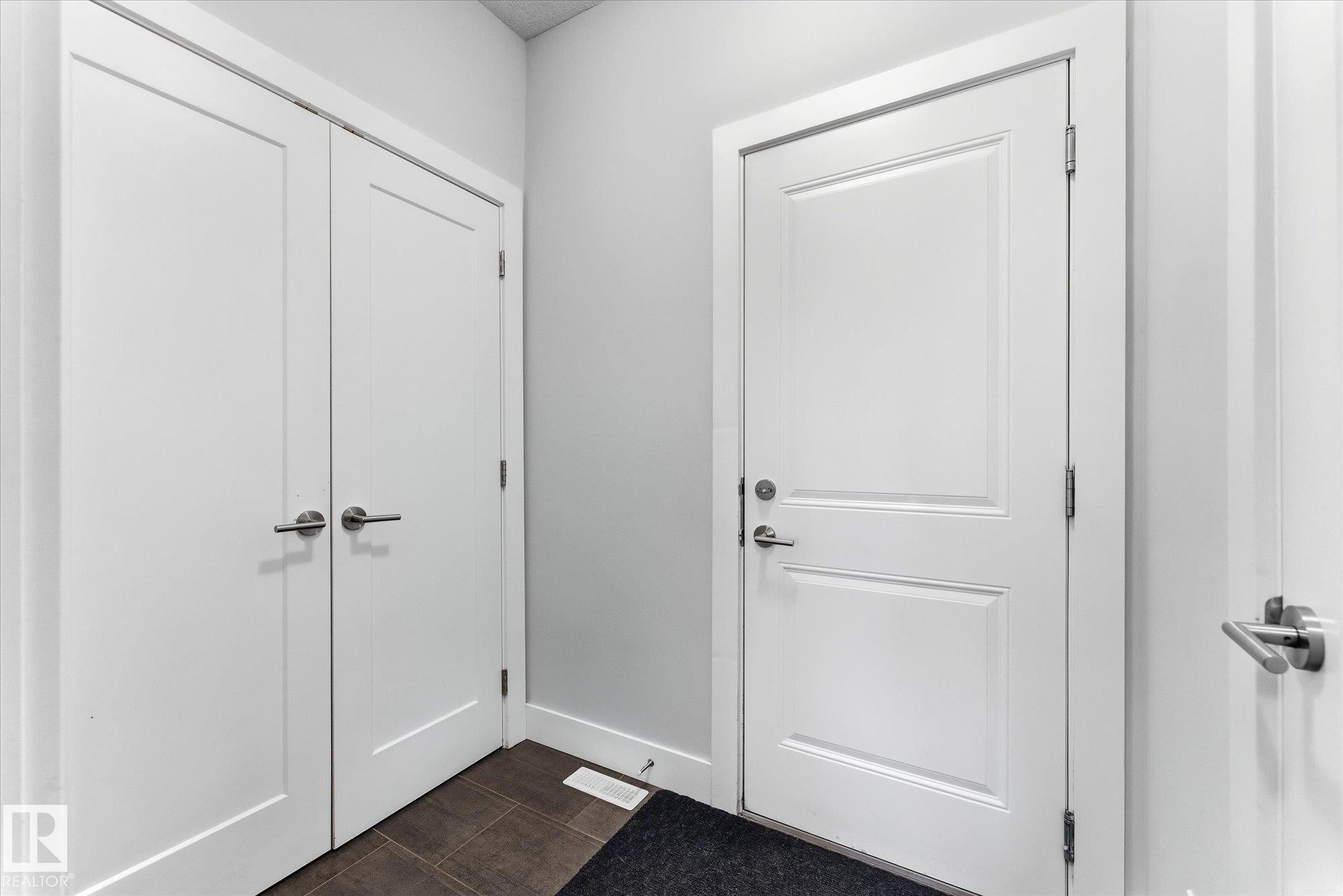 White two-panel doors with satin nickel hardware and dark tile flooring - #15 4835 Wright Dr Sw, Edmonton, AB