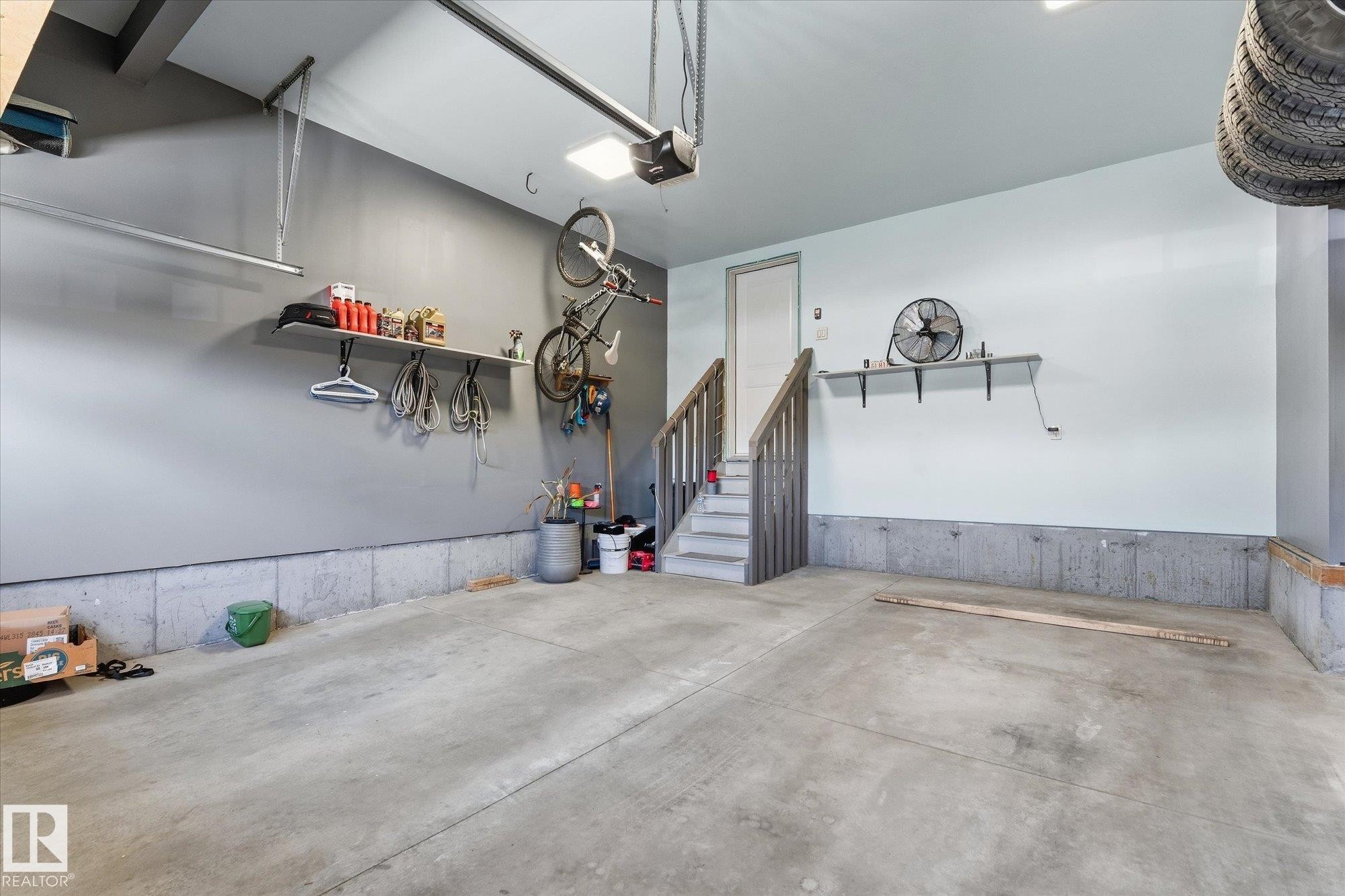 Concrete flooring with partial wall paneling, built-in shelving, and interior access stairs with wooden railings - #15 4835 Wright Dr Sw, Edmonton, AB