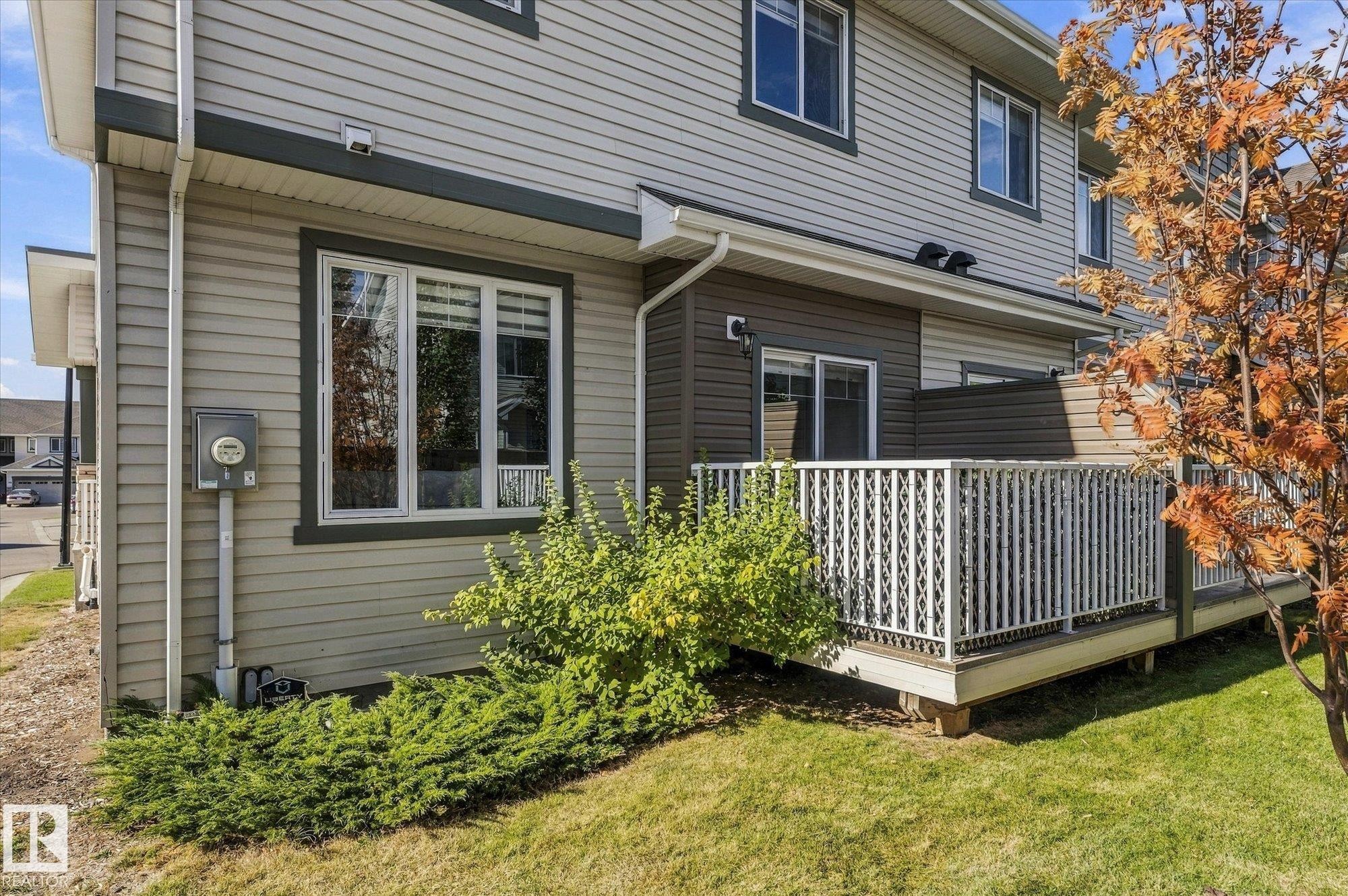 Rear exterior featuring multi-level siding, a private deck with white railing, and a sliding glass door - #15 4835 Wright Dr Sw, Edmonton, AB