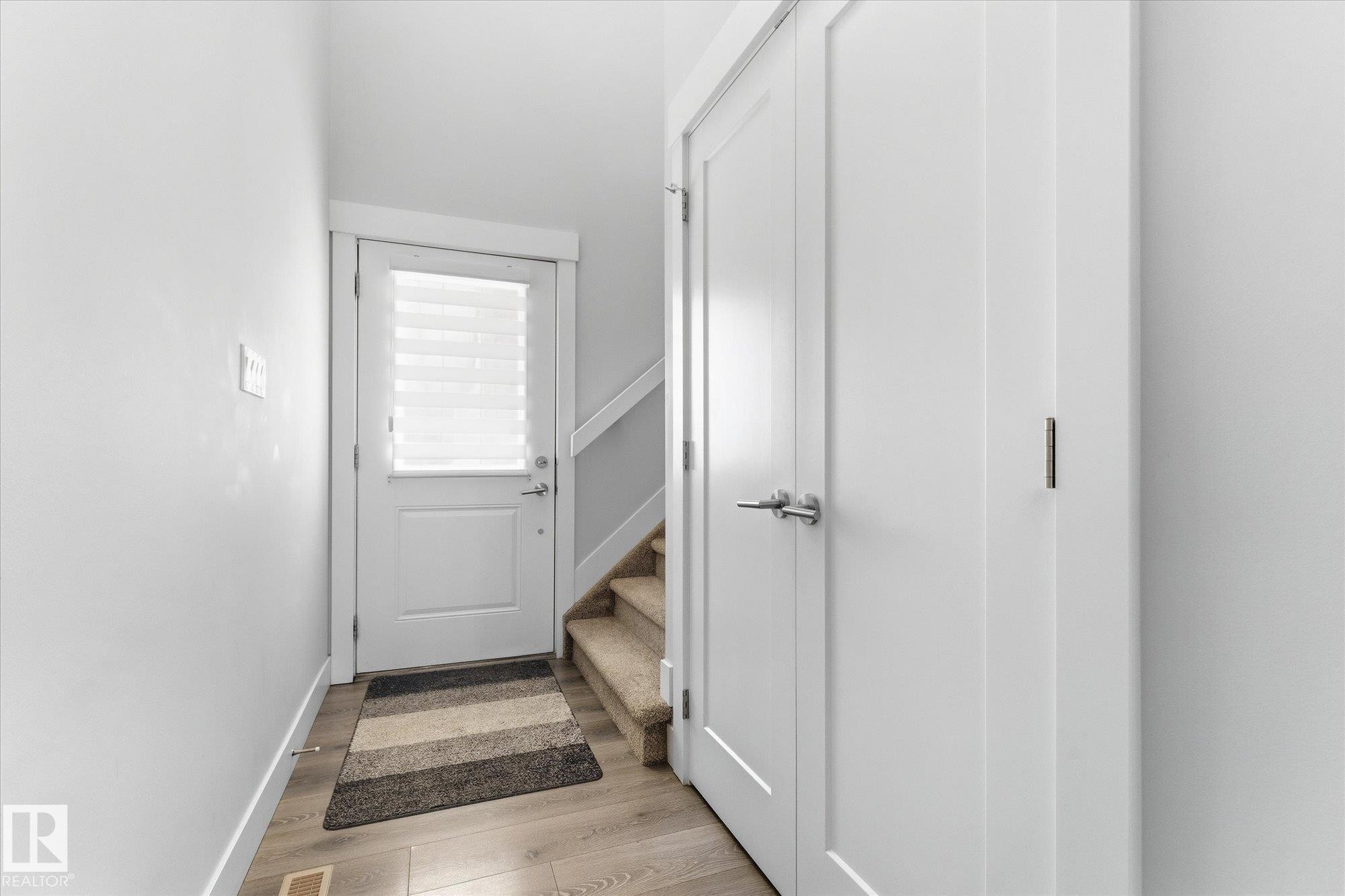 White interior doors with brushed nickel hardware, wood-finish flooring, and a carpeted staircase - #15 4835 Wright Dr Sw, Edmonton, AB