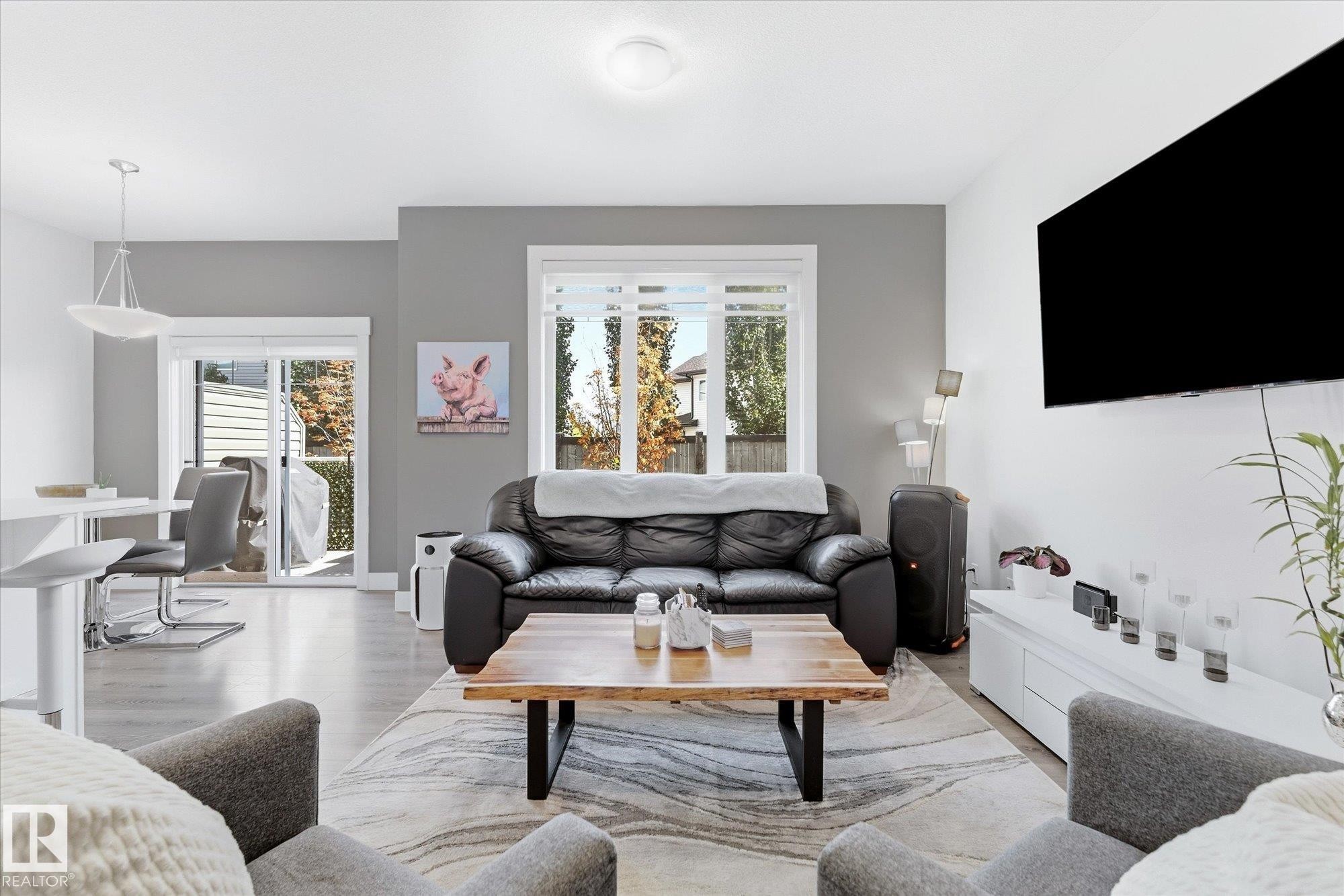 Open-concept living area with light wood-finish flooring, white walls, and a grey accent wall - #15 4835 Wright Dr Sw, Edmonton, AB