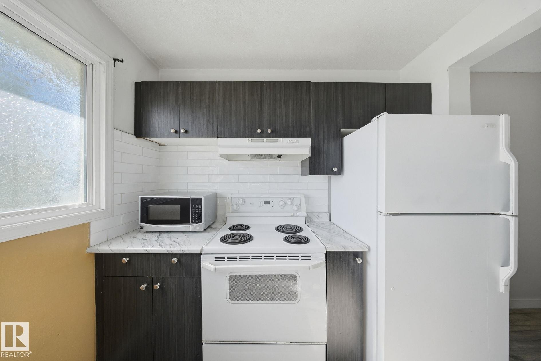 Kitchen featuring dark wood-finish cabinetry, white subway tile backsplash, light-colored countertops, white refrigerator, and white range - 164 Dickinsfield Court Nw, Edmonton, AB