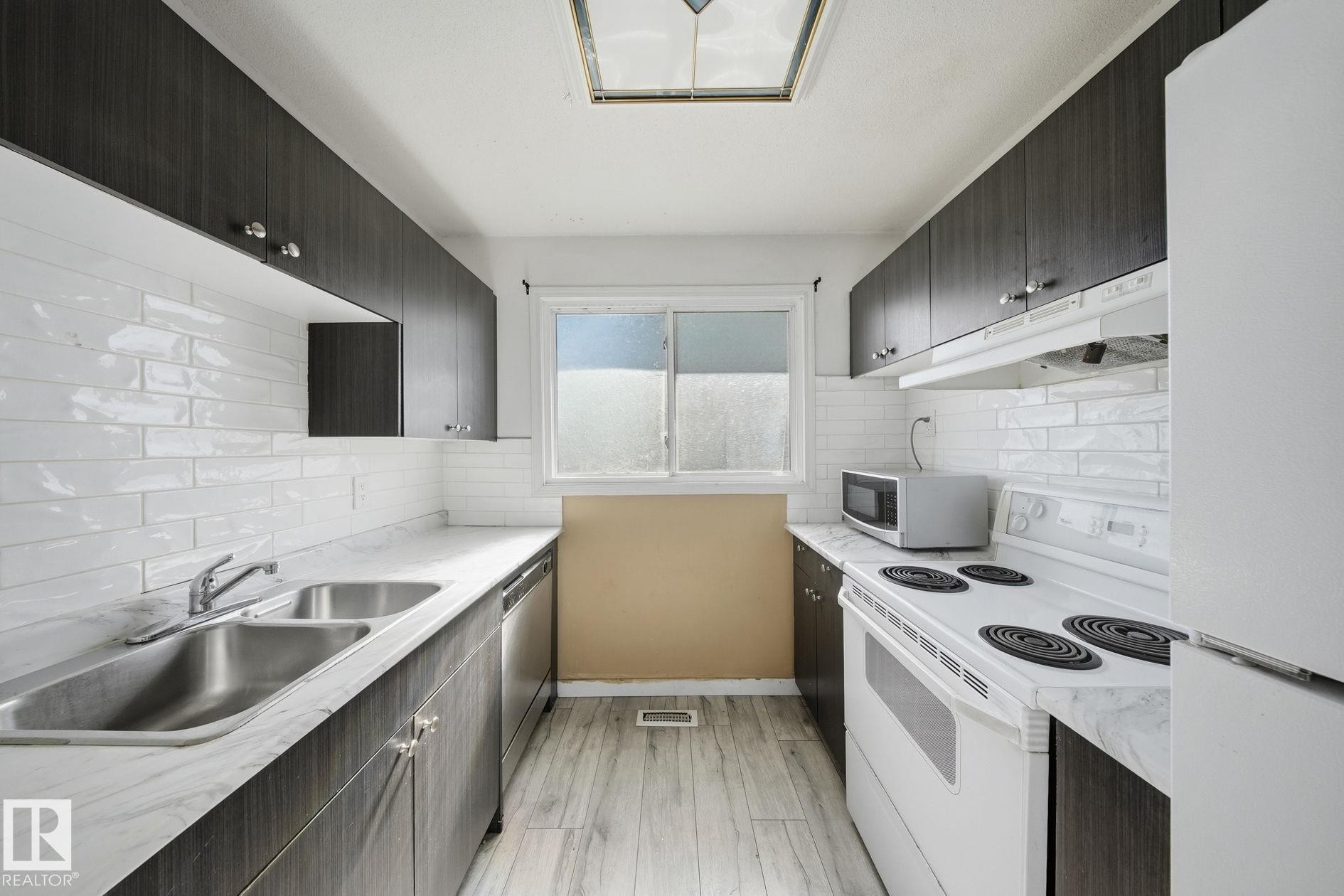 Galley kitchen featuring dark wood-finish cabinetry, white subway tile backsplash, and light-toned countertops - 164 Dickinsfield Court Nw, Edmonton, AB