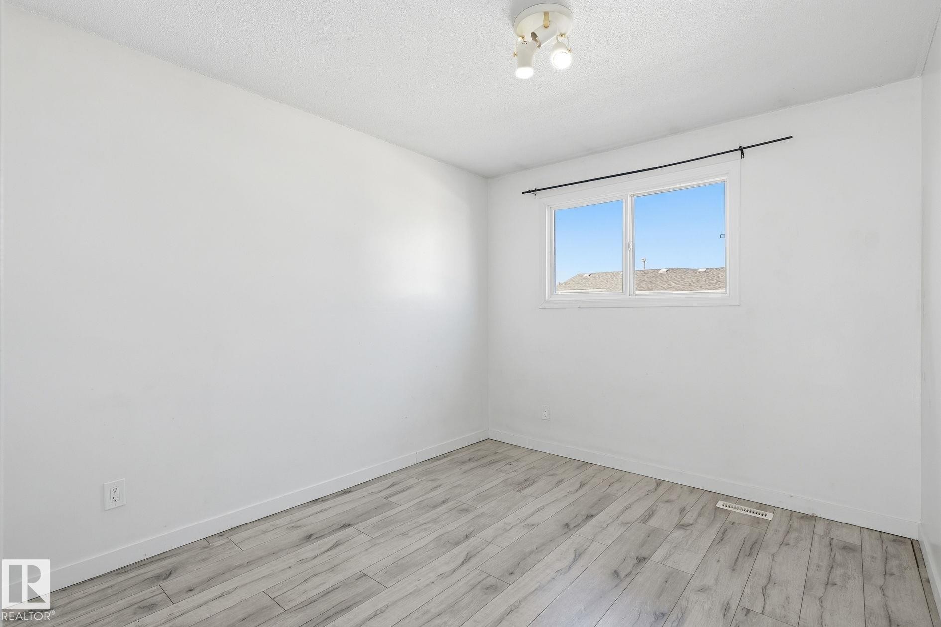 Window with a black curtain rod, wood-finish flooring, and a ceiling-mounted light fixture - 164 Dickinsfield Court Nw, Edmonton, AB
