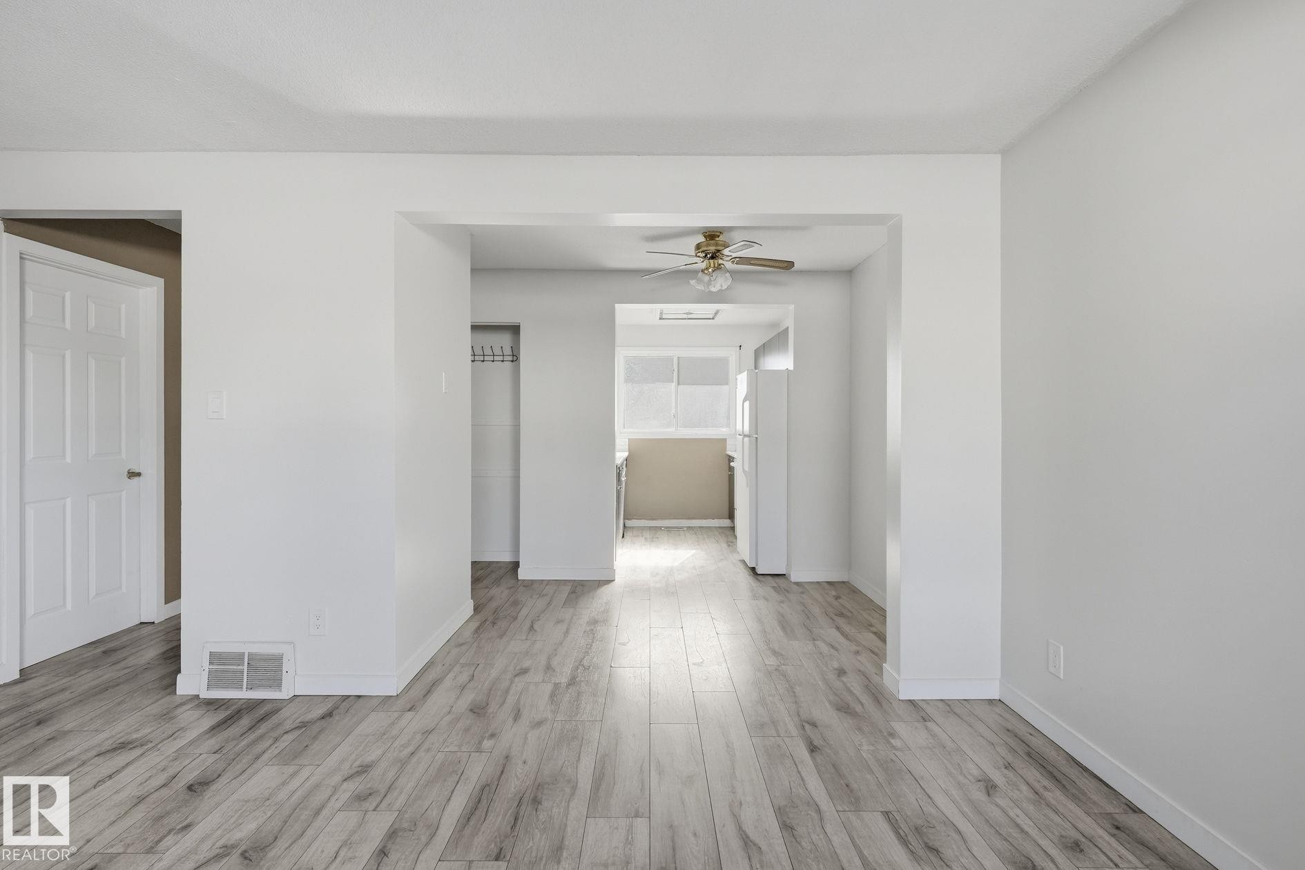 Updated wood-finish flooring throughout, bright white walls, a ceiling fan fixture, and a kitchen with white appliances - 164 Dickinsfield Court Nw, Edmonton, AB