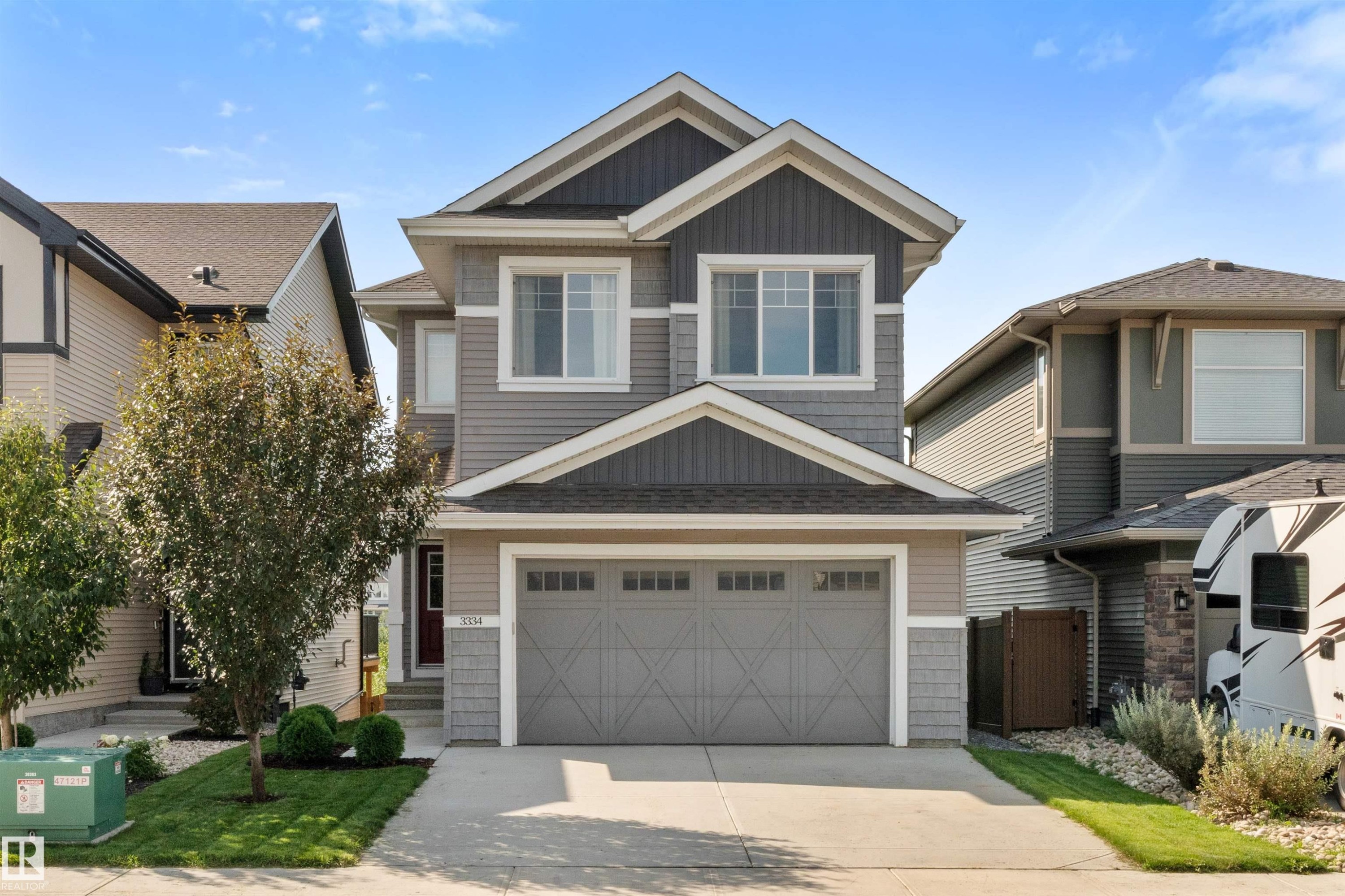 Multi-textured exterior siding, attached garage, concrete driveway, front entry with transom window, and mature landscaping - 3334 Parker Loop Sw, Edmonton, AB