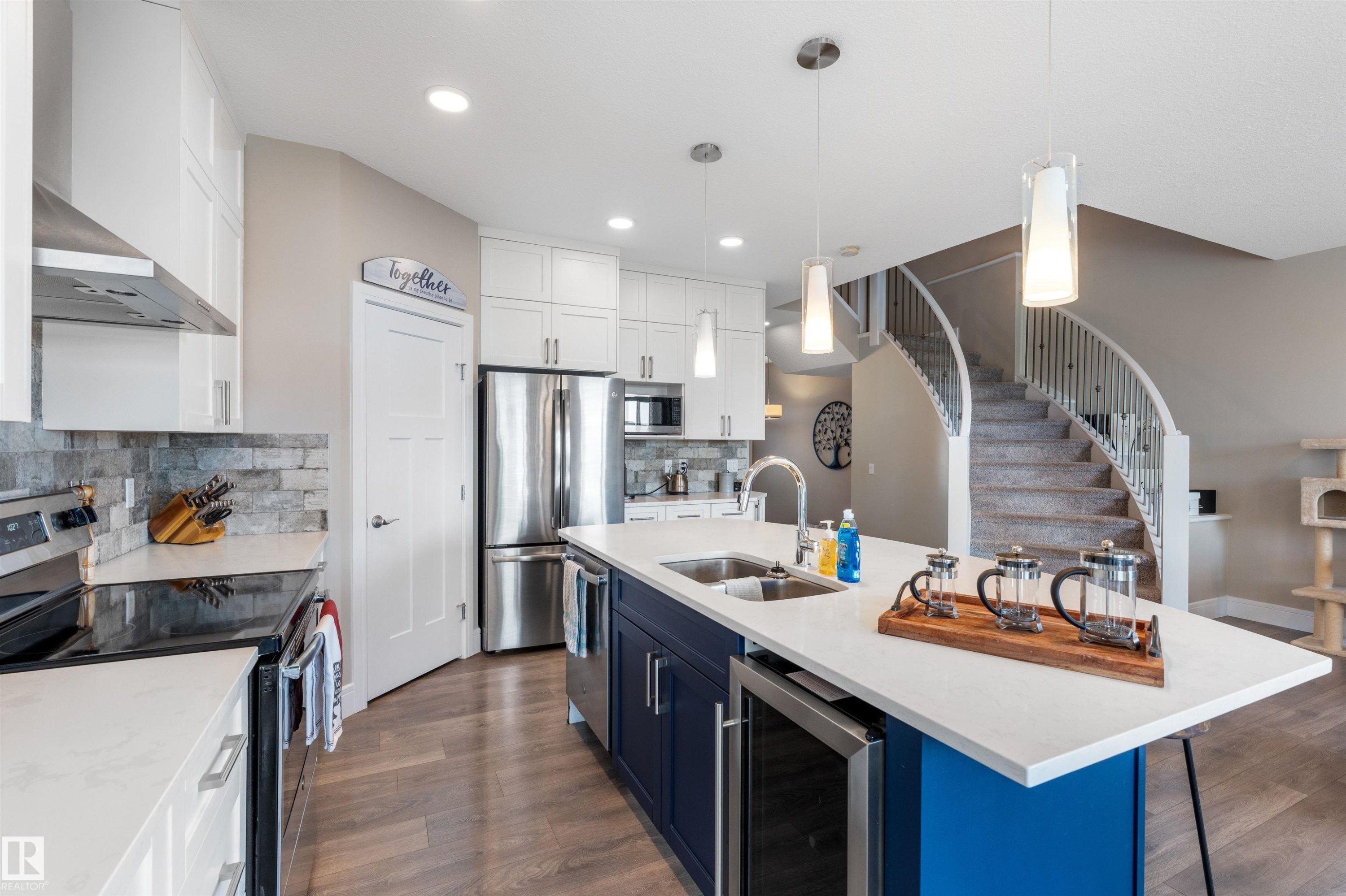 Modern kitchen with white cabinetry, stainless steel appliances, and a blue island featuring a beverage cooler - 3334 Parker Loop Sw, Edmonton, AB
