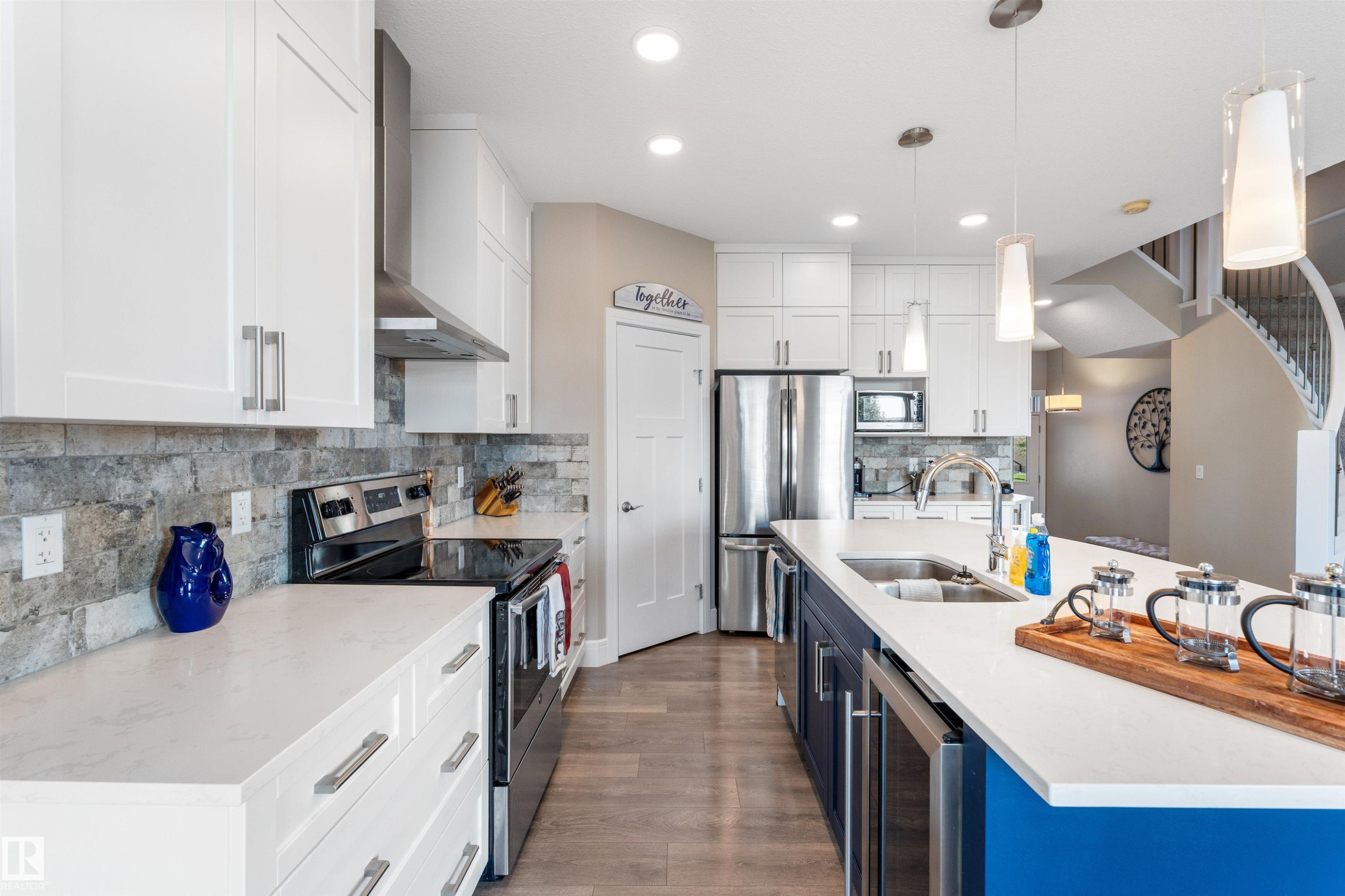 Modern kitchen featuring white cabinetry, stone-look backsplash, stainless steel appliances, and a central island with a built-in sink - 3334 Parker Loop Sw, Edmonton, AB