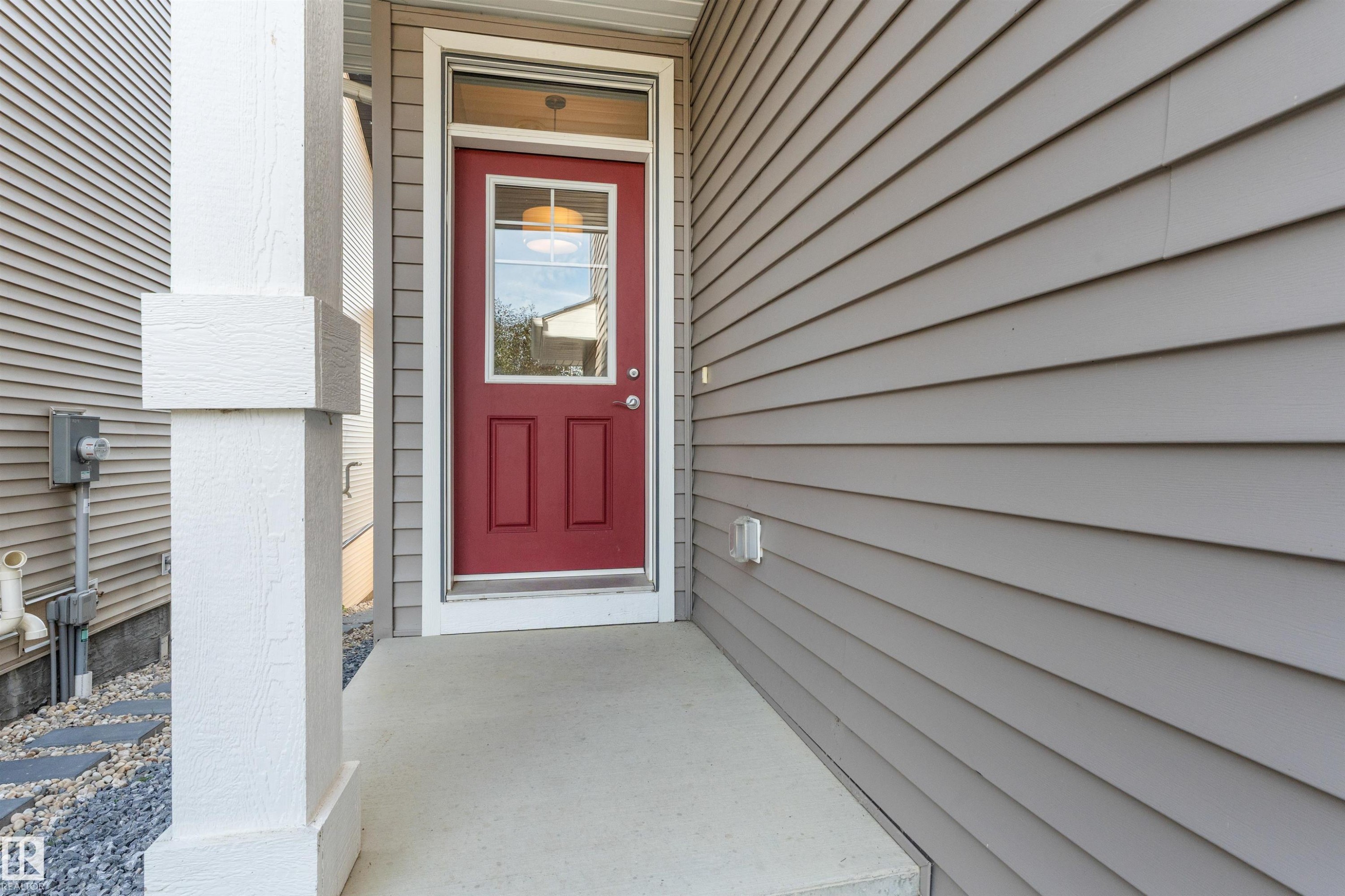 Red entry door with an overhead transom window, concrete porch, and white structural column - 3334 Parker Loop Sw, Edmonton, AB