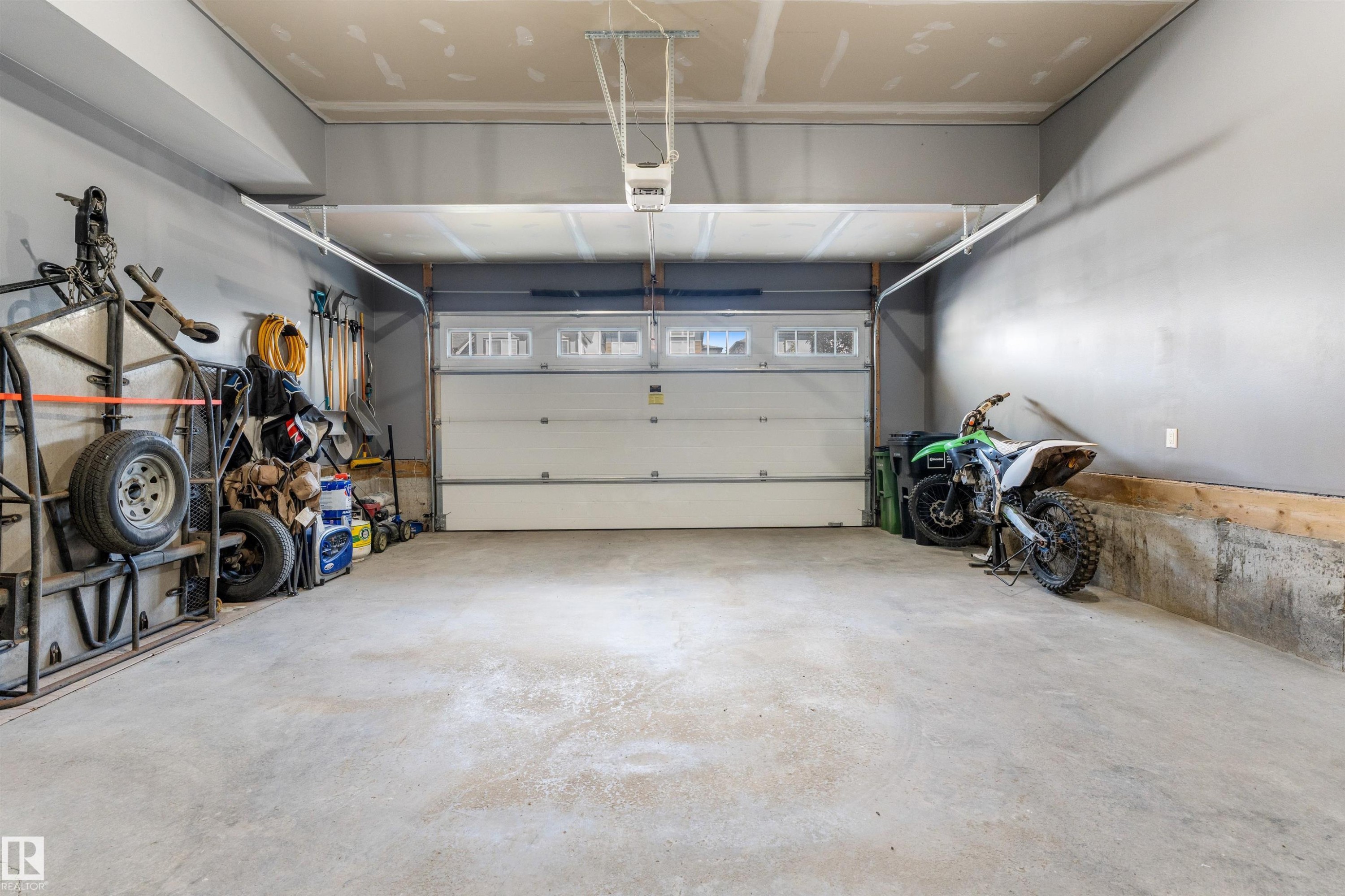 Spacious garage with a concrete floor, painted gray walls, and a white overhead door with upper window inserts - 3334 Parker Loop Sw, Edmonton, AB