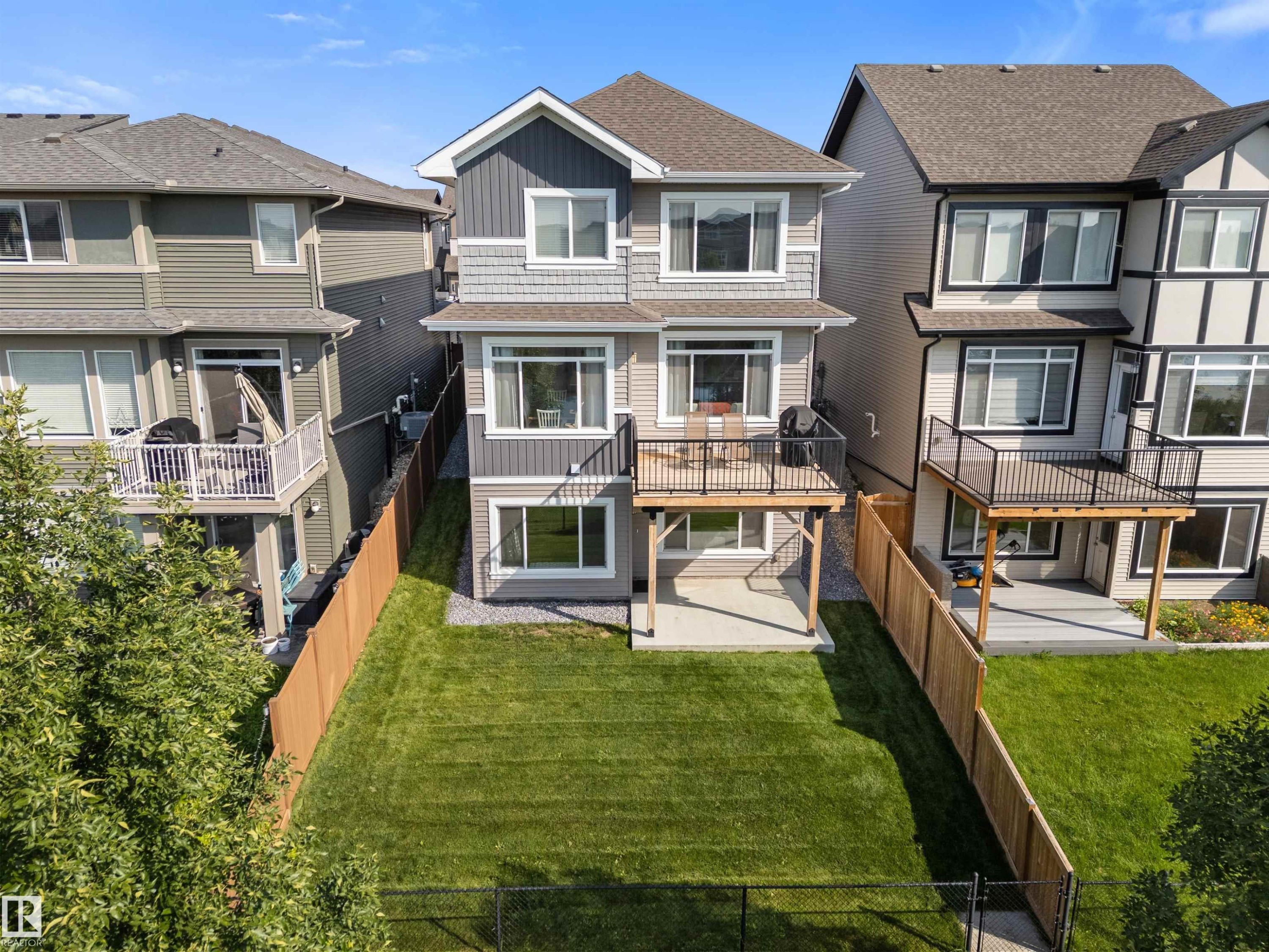 Multi-level rear exterior with a second-story deck featuring dark railings, a ground-level patio, and a fenced lawn area - 3334 Parker Loop Sw, Edmonton, AB