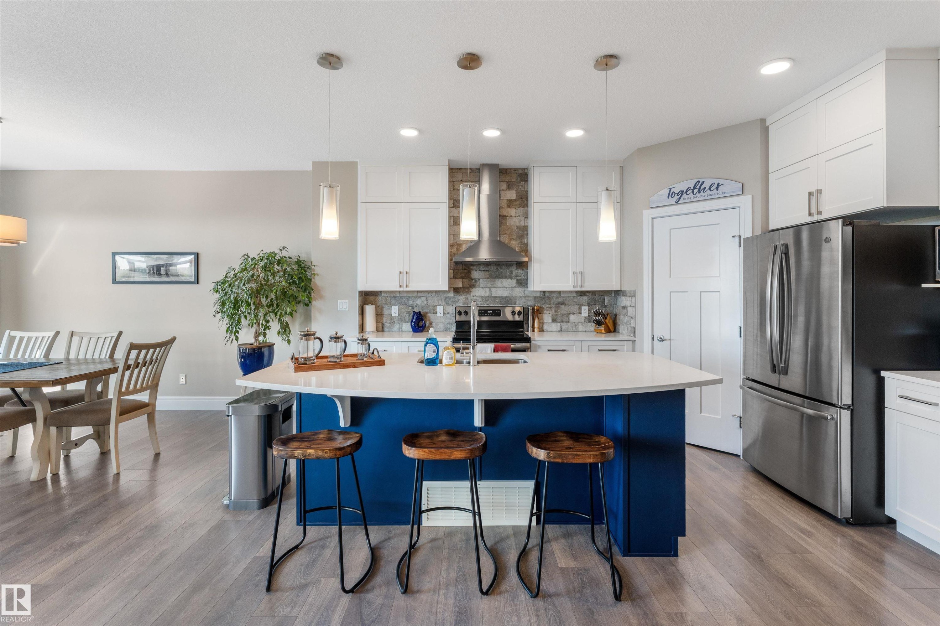 Kitchen featuring an oversized island with a curved countertop, pendant lighting, stainless steel appliances, and wood-finish flooring - 3334 Parker Loop Sw, Edmonton, AB
