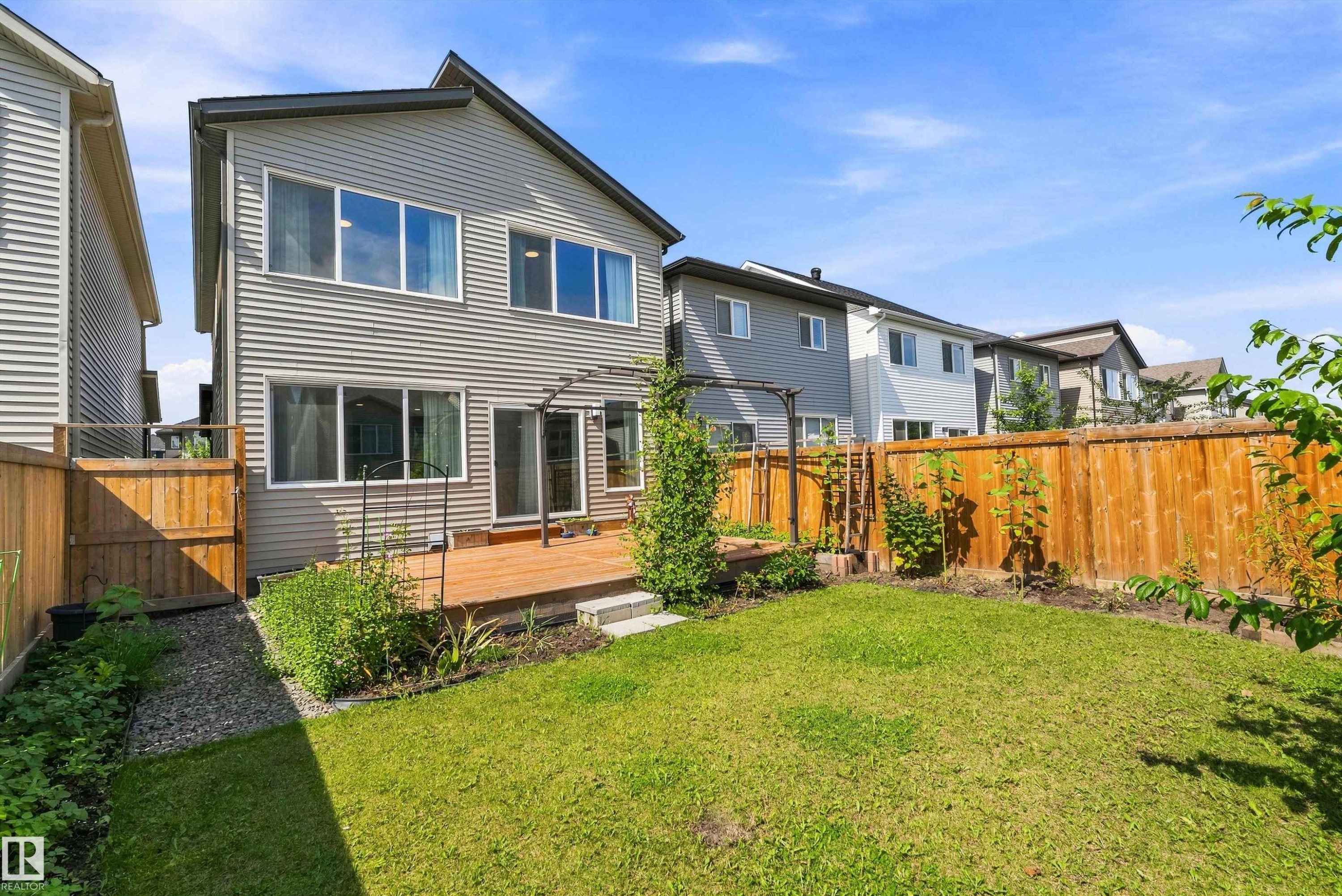 Rear exterior featuring siding, upper and lower windows, a ground-level wood deck, and a fenced yard with lawn - 9227 223 Street Nw, Edmonton, AB