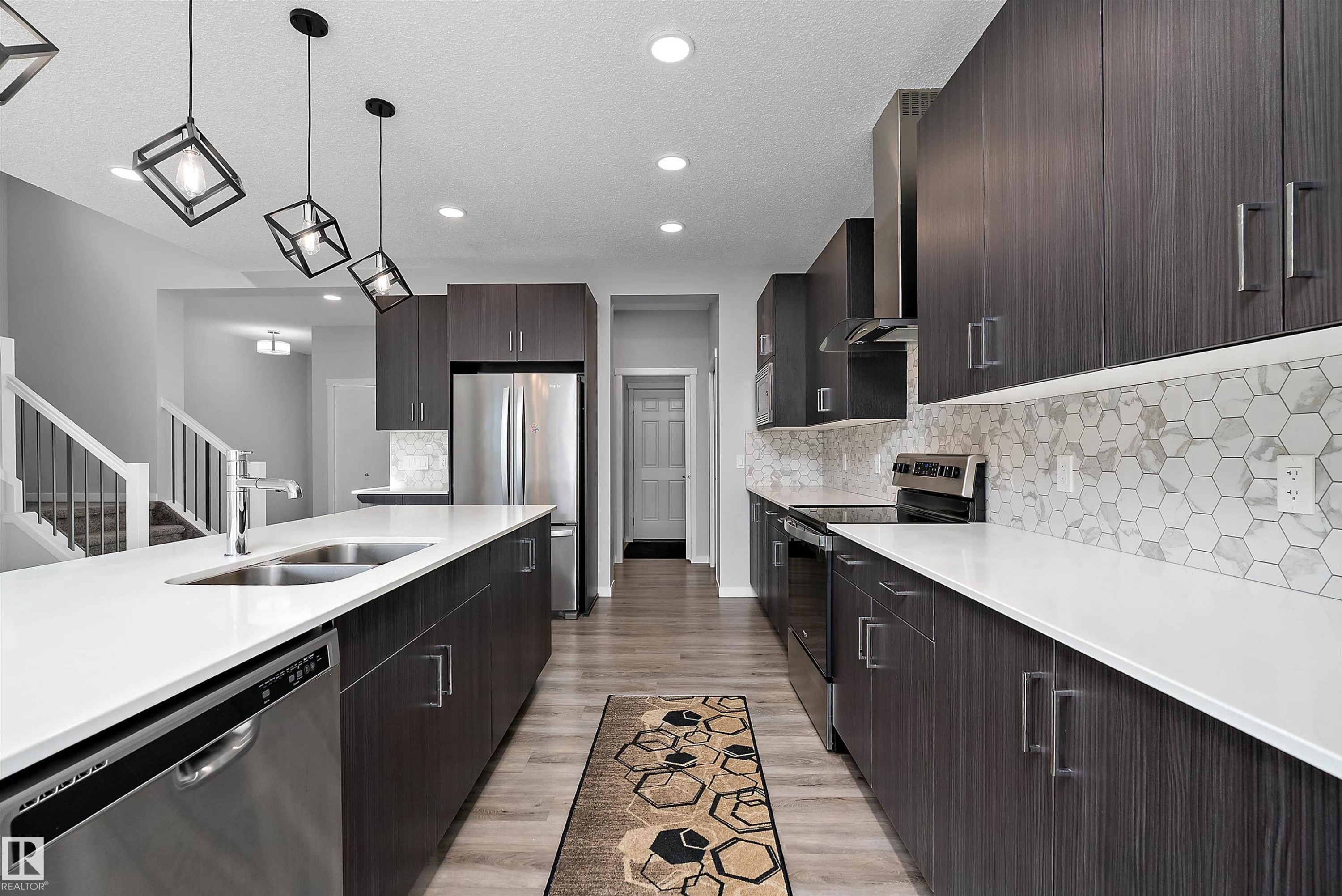 Kitchen featuring dark wood-finish cabinetry, white countertops, stainless steel appliances, and a hexagonal tile backsplash - 9227 223 Street Nw, Edmonton, AB