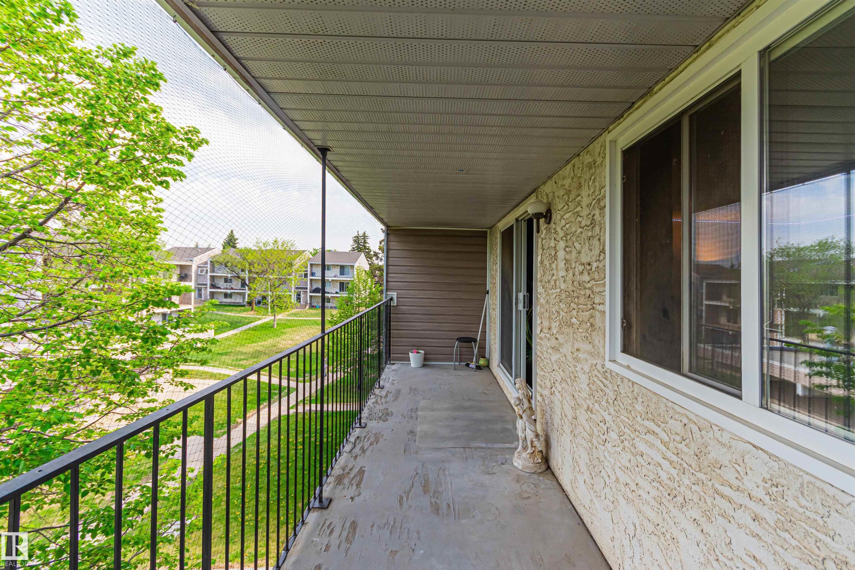 Private balcony with textured stucco exterior, sliding patio door, and white frame windows - #6 3819 76 St Nw, Edmonton, AB