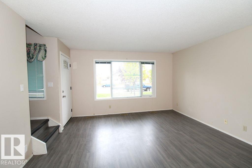 Spacious room featuring wood-finish flooring, neutral-toned walls, and a large window with white trim - 11393 22 Avenue Nw, Edmonton, AB