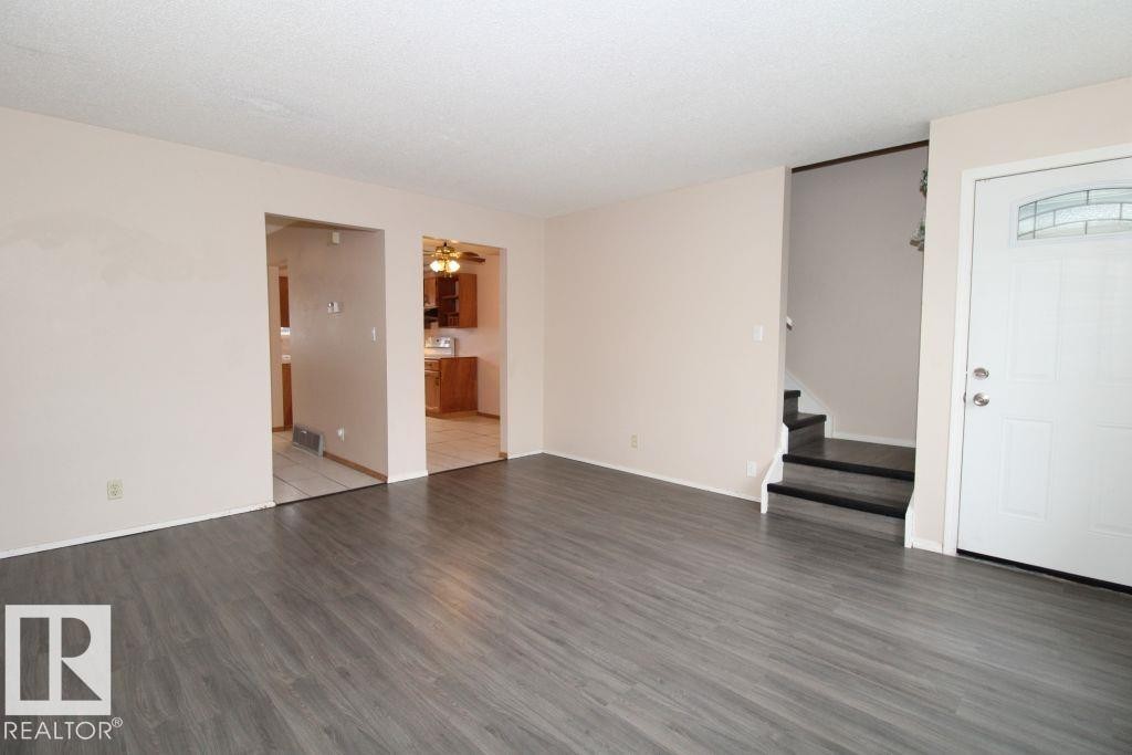Gray wood-finish flooring, white entry door with decorative glass, and a neutral wall color throughout - 11393 22 Avenue Nw, Edmonton, AB