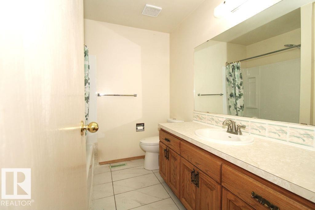 Bathroom featuring a wood-finish vanity with an integrated sink, a large wall-mounted mirror, and tile flooring - 11393 22 Avenue Nw, Edmonton, AB