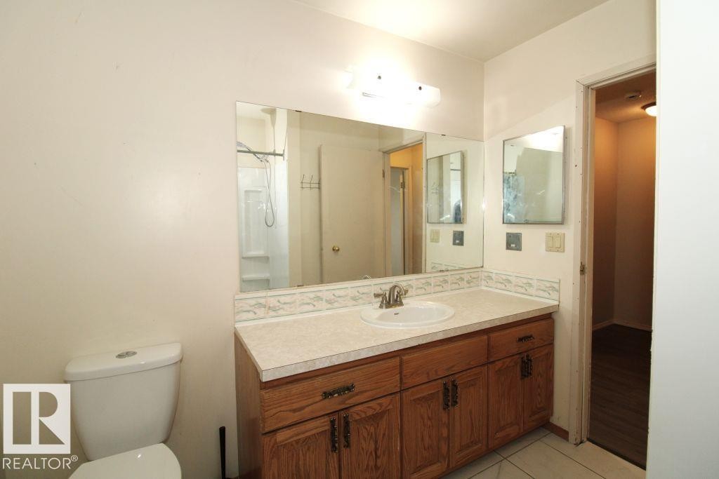 White ceramic toilet, vanity with wood-finish cabinetry, solid surface countertop, integrated sink, and wall-mounted mirror - 11393 22 Avenue Nw, Edmonton, AB