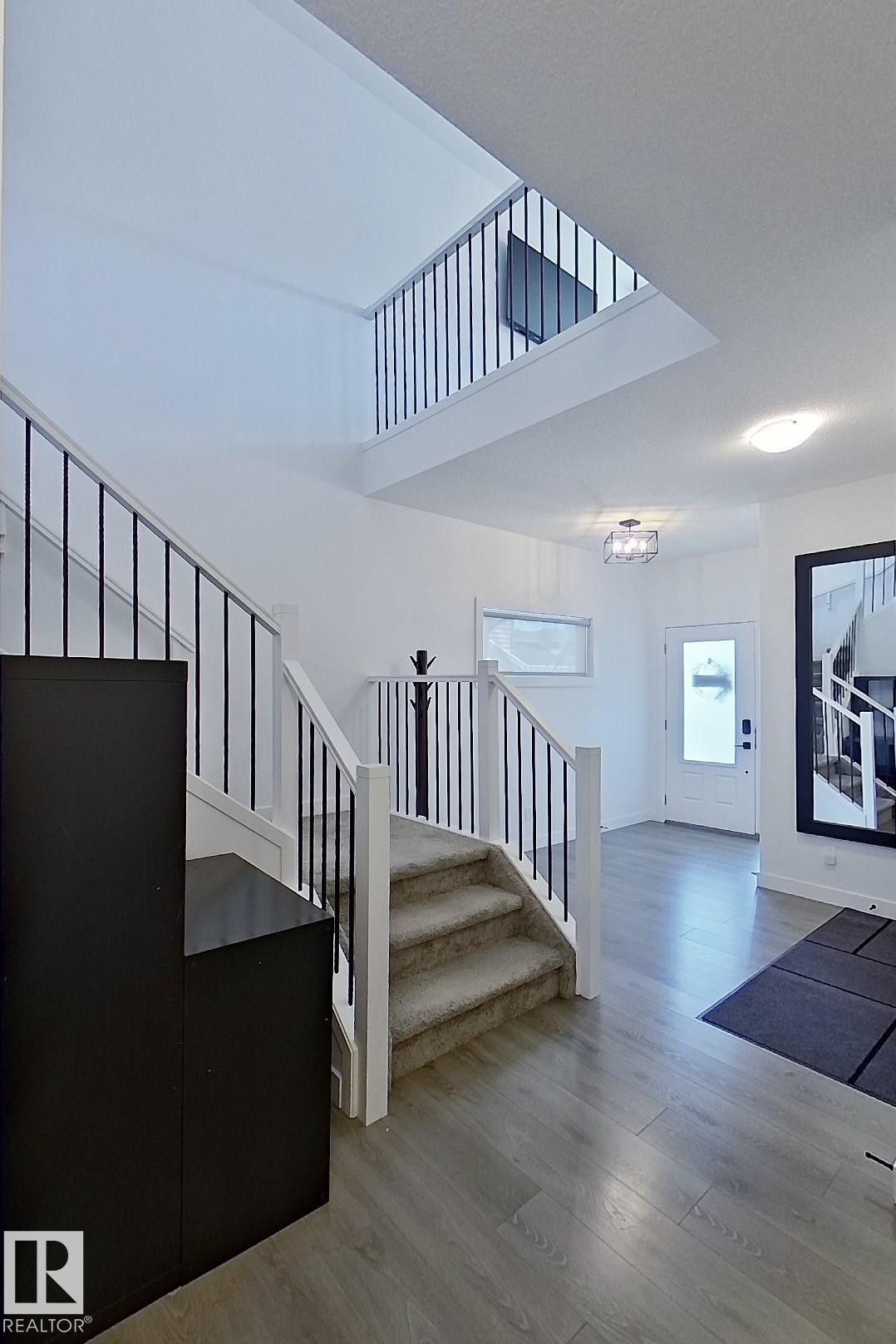 Two-story foyer with wood-finish flooring, carpeted stairs, and a multi-level open baluster railing system - 40 Jamison Crescent, St. Albert, AB