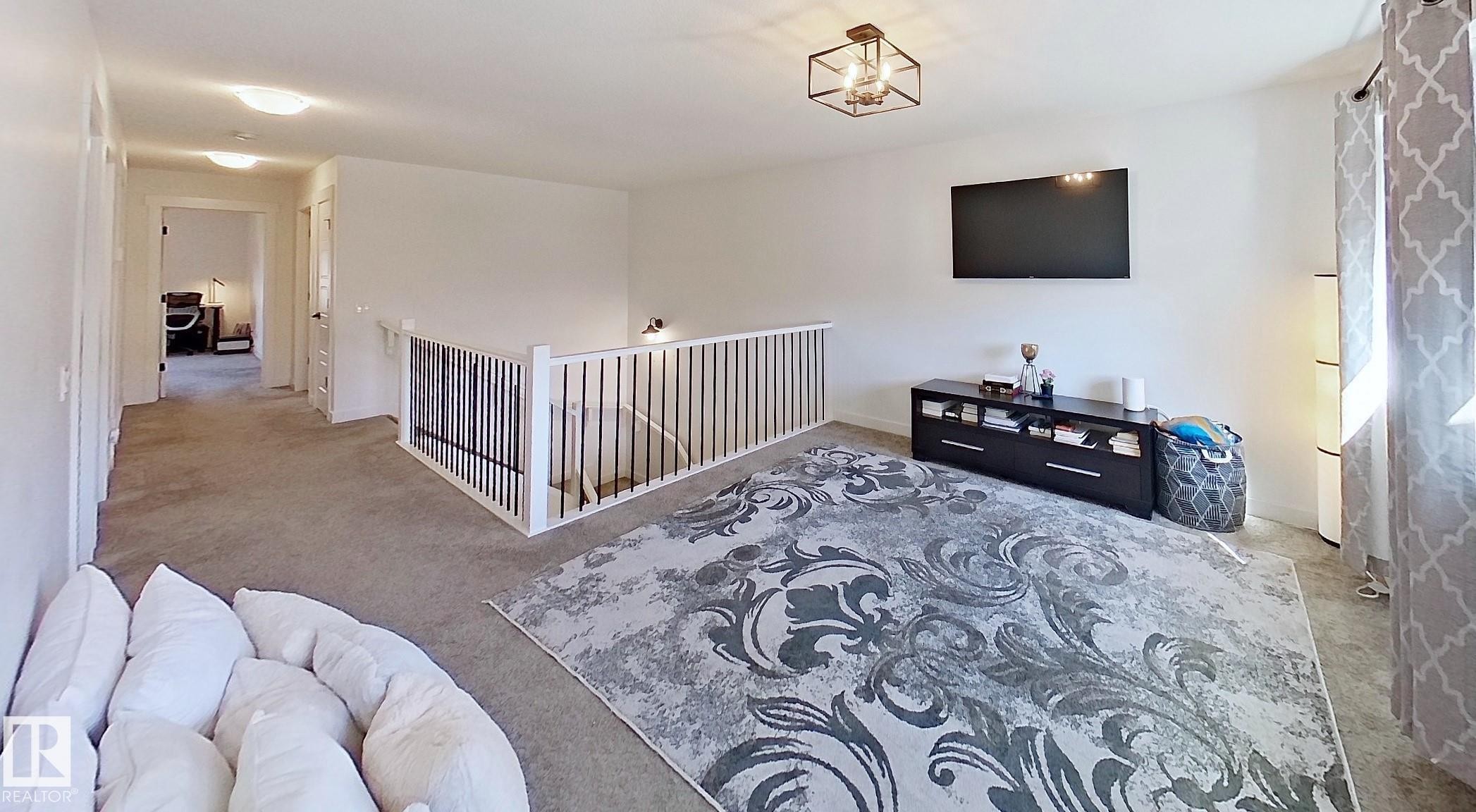 Carpeted open-concept bonus room featuring a metal and wood railing, recessed lighting, and a contemporary ceiling fixture - 40 Jamison Crescent, St. Albert, AB