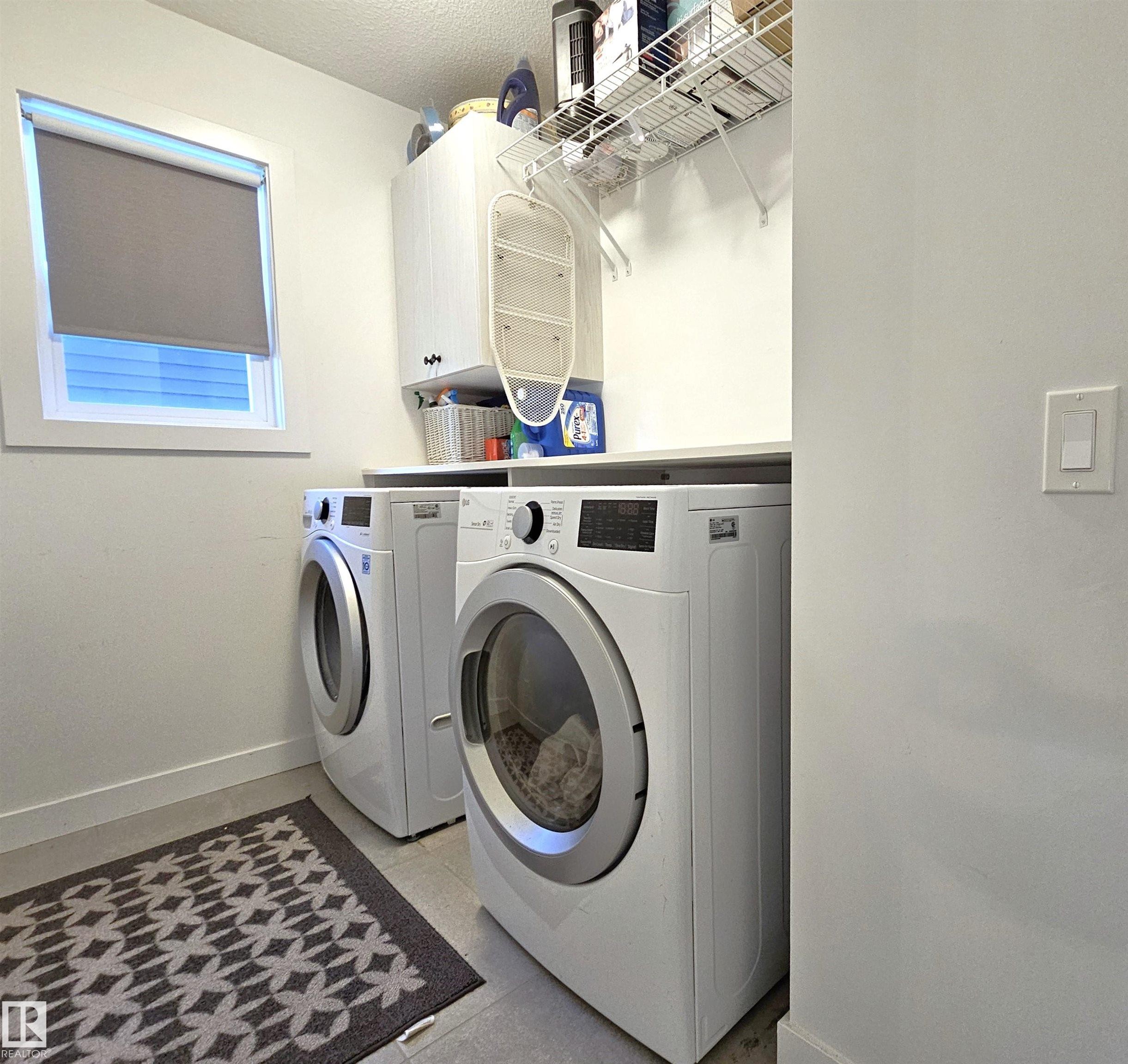 Laundry area featuring side-by-side appliances, built-in upper cabinetry, open shelving, a window, and durable flooring - 40 Jamison Crescent, St. Albert, AB