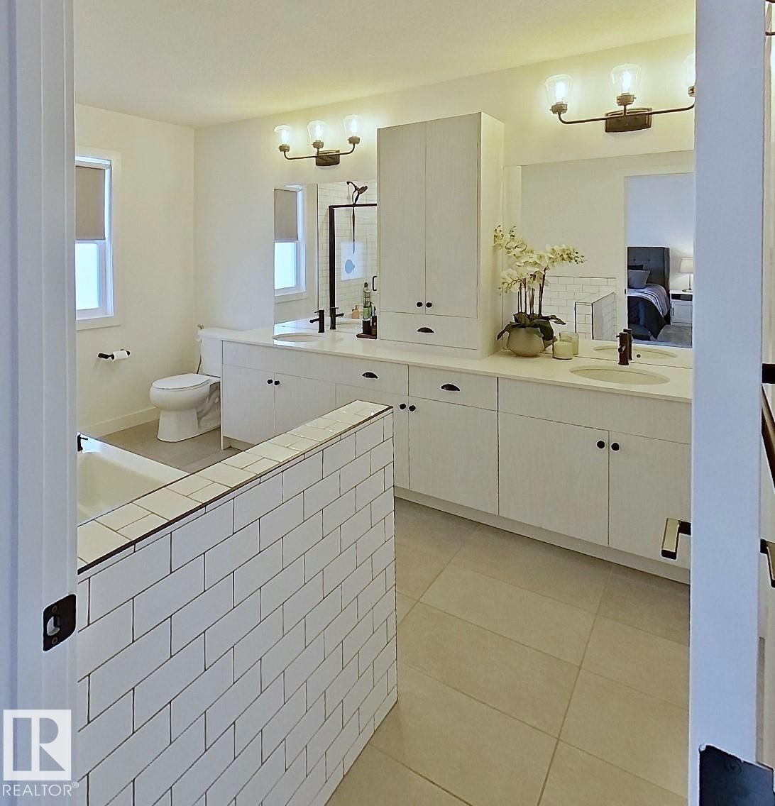White subway tile partial wall, dual vanity with undermount sinks, white cabinetry, dark bronze hardware, and tile flooring - 40 Jamison Crescent, St. Albert, AB