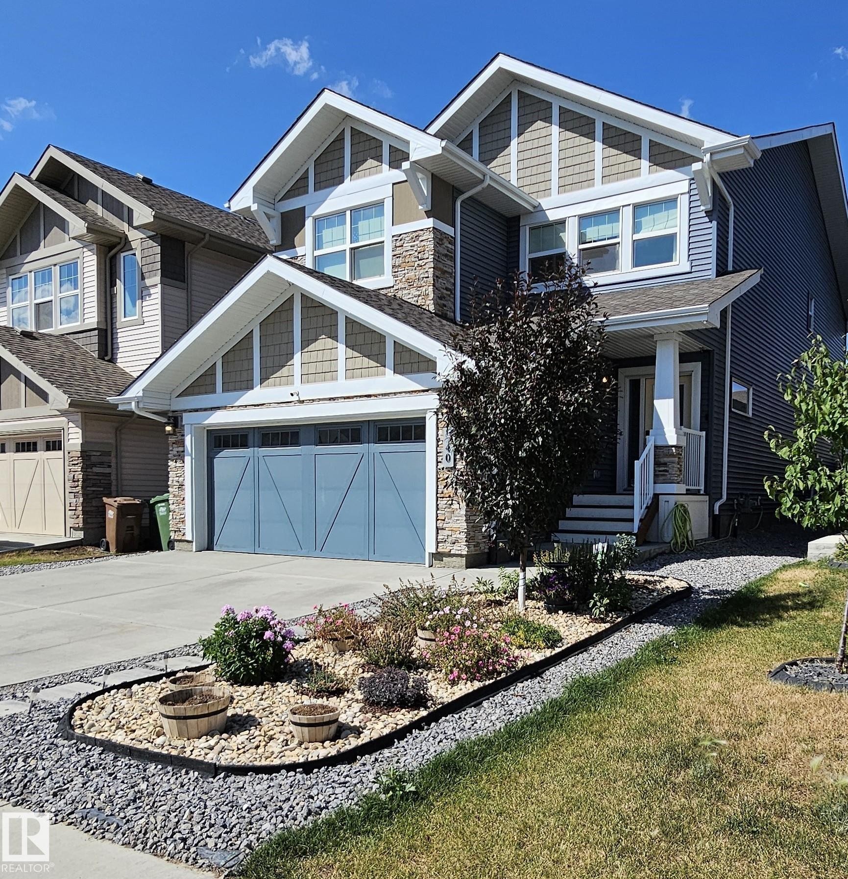 Multi-gabled exterior with shingle and stone accents, concrete driveway, attached two-car garage, and a landscaped front garden with a rock border - 40 Jamison Crescent, St. Albert, AB