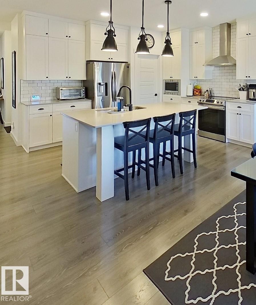 Kitchen featuring light wood-finish flooring, white cabinetry, a center island with seating, stainless steel appliances, and subway tile backsplash - 40 Jamison Crescent, St. Albert, AB