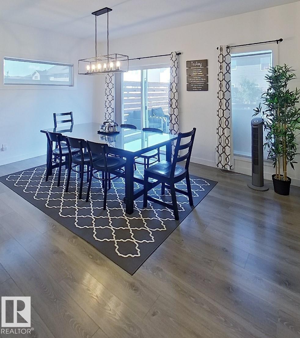 Wood-finish flooring throughout, complemented by a large sliding glass door, a horizontal transom window, and a modern rectangular chandelier - 40 Jamison Crescent, St. Albert, AB