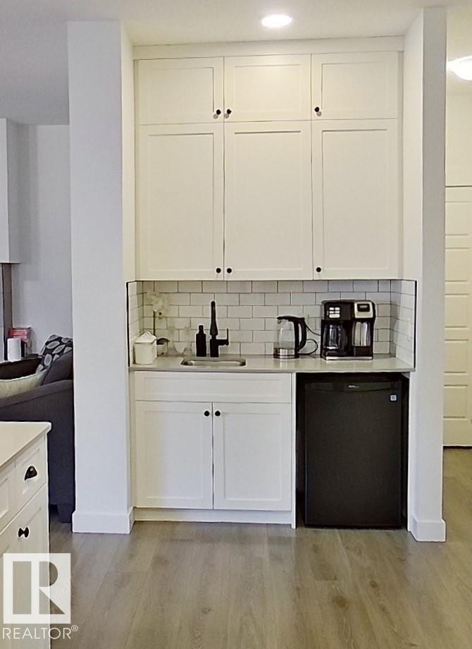 Built-in wet bar featuring white shaker-style cabinetry, a subway tile backsplash, a matte black faucet, and wood-finish flooring - 40 Jamison Crescent, St. Albert, AB