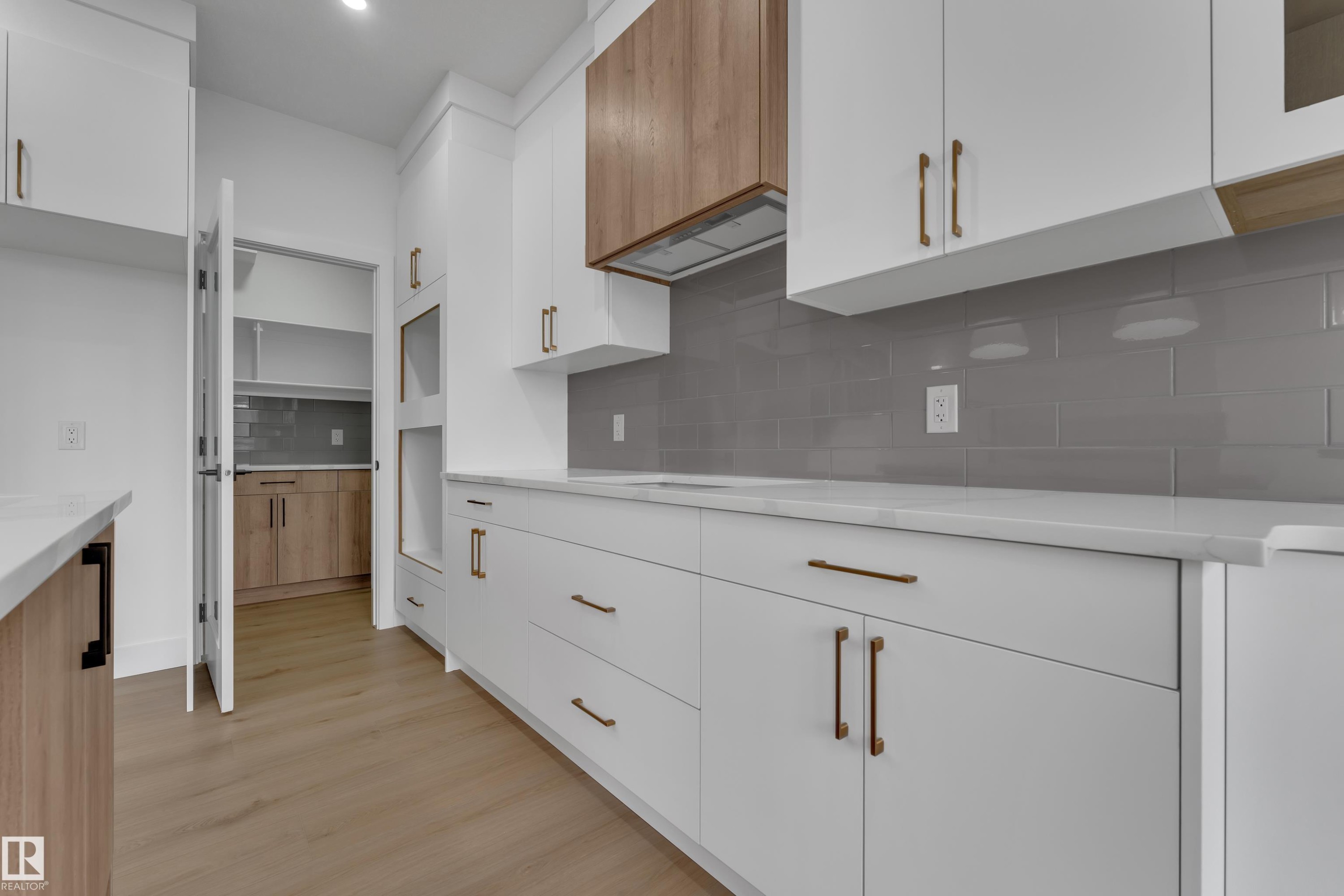 Contemporary kitchen featuring white cabinetry, wood-finish accents, light countertops, and a gray subway tile backsplash - 178 Munn Way, Leduc, AB